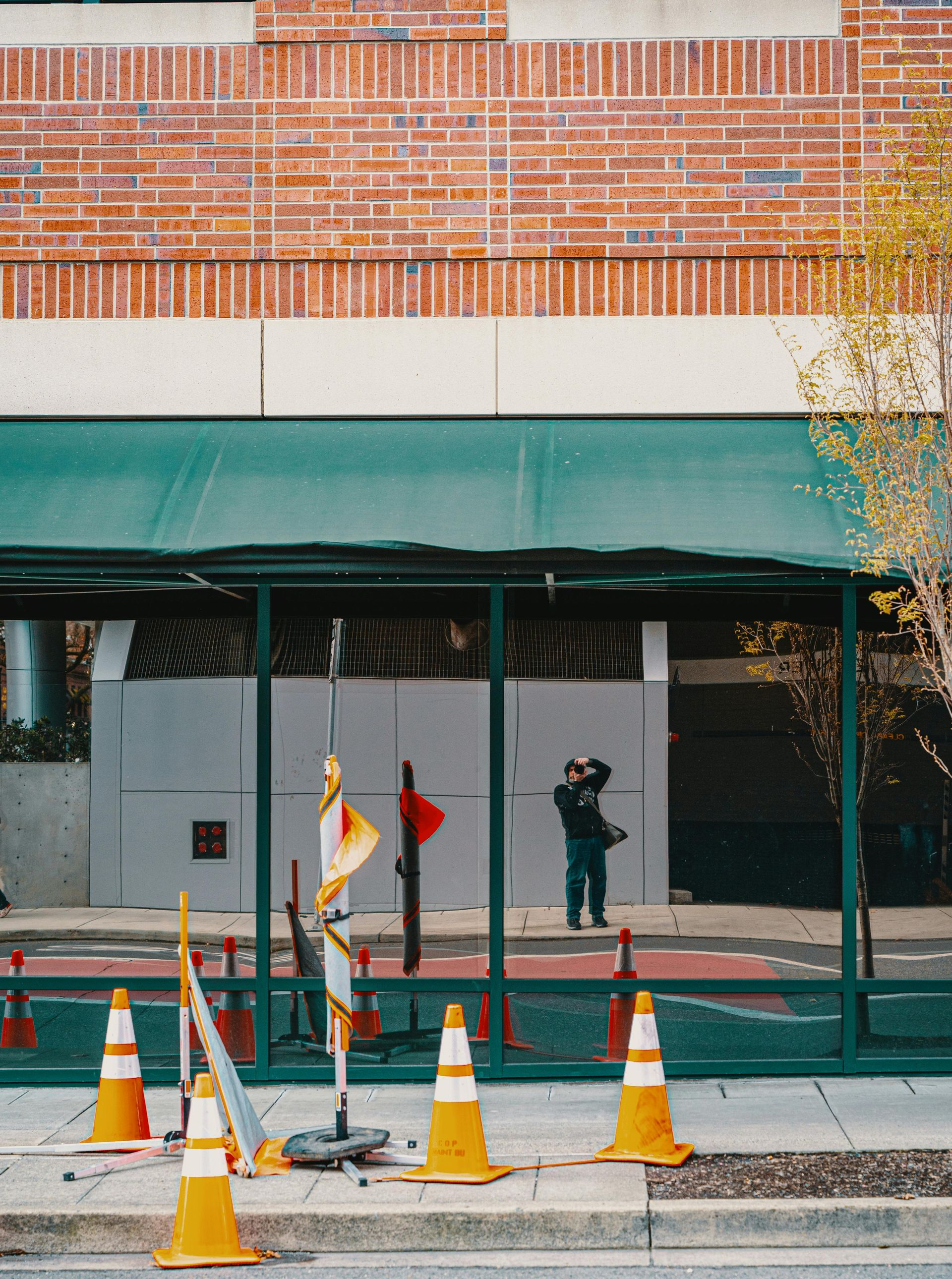 Construction cones and barriers in front of a building with green awning and reflective glass.