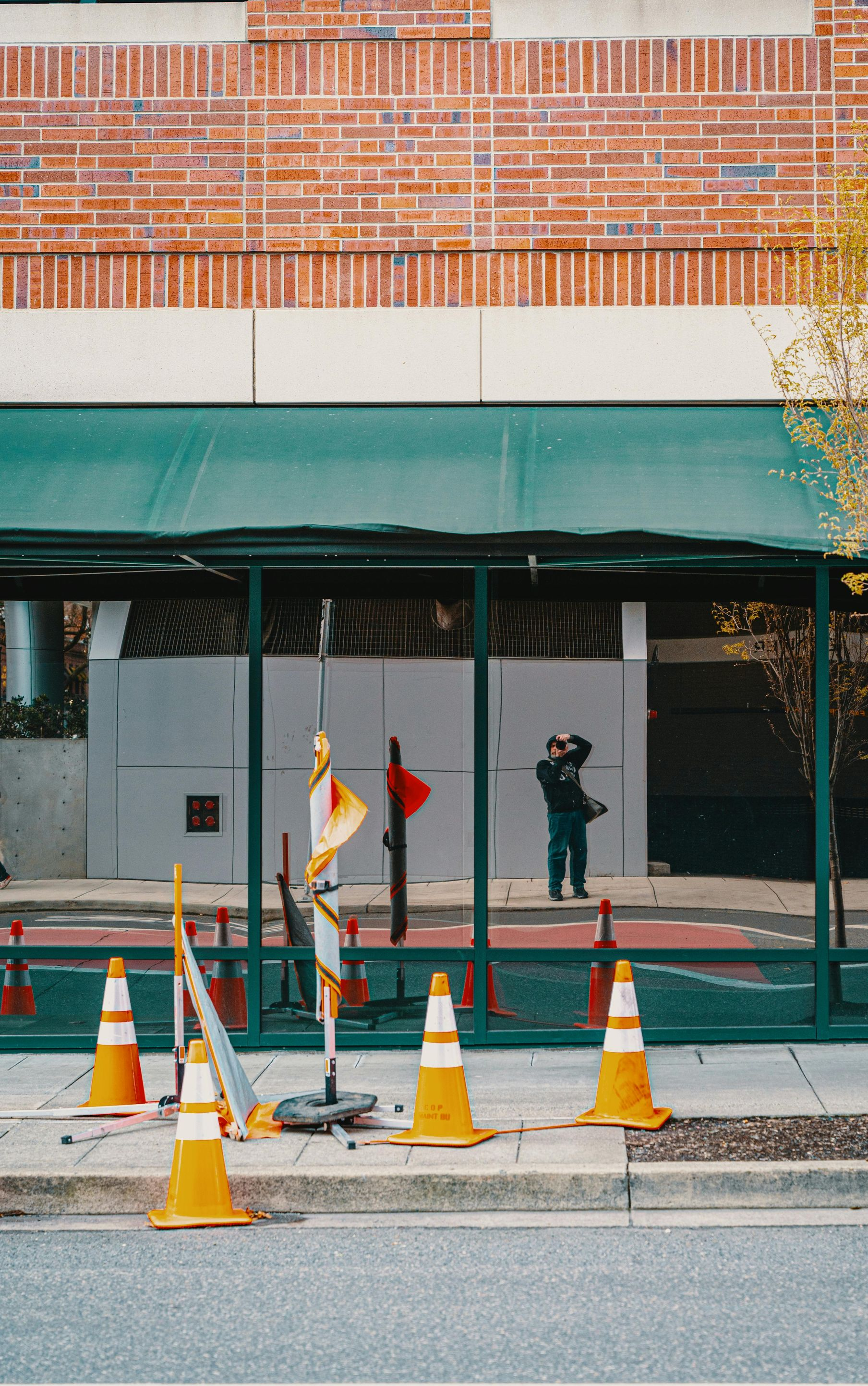 Construction cones and barriers in front of a building with green awning and reflective glass.