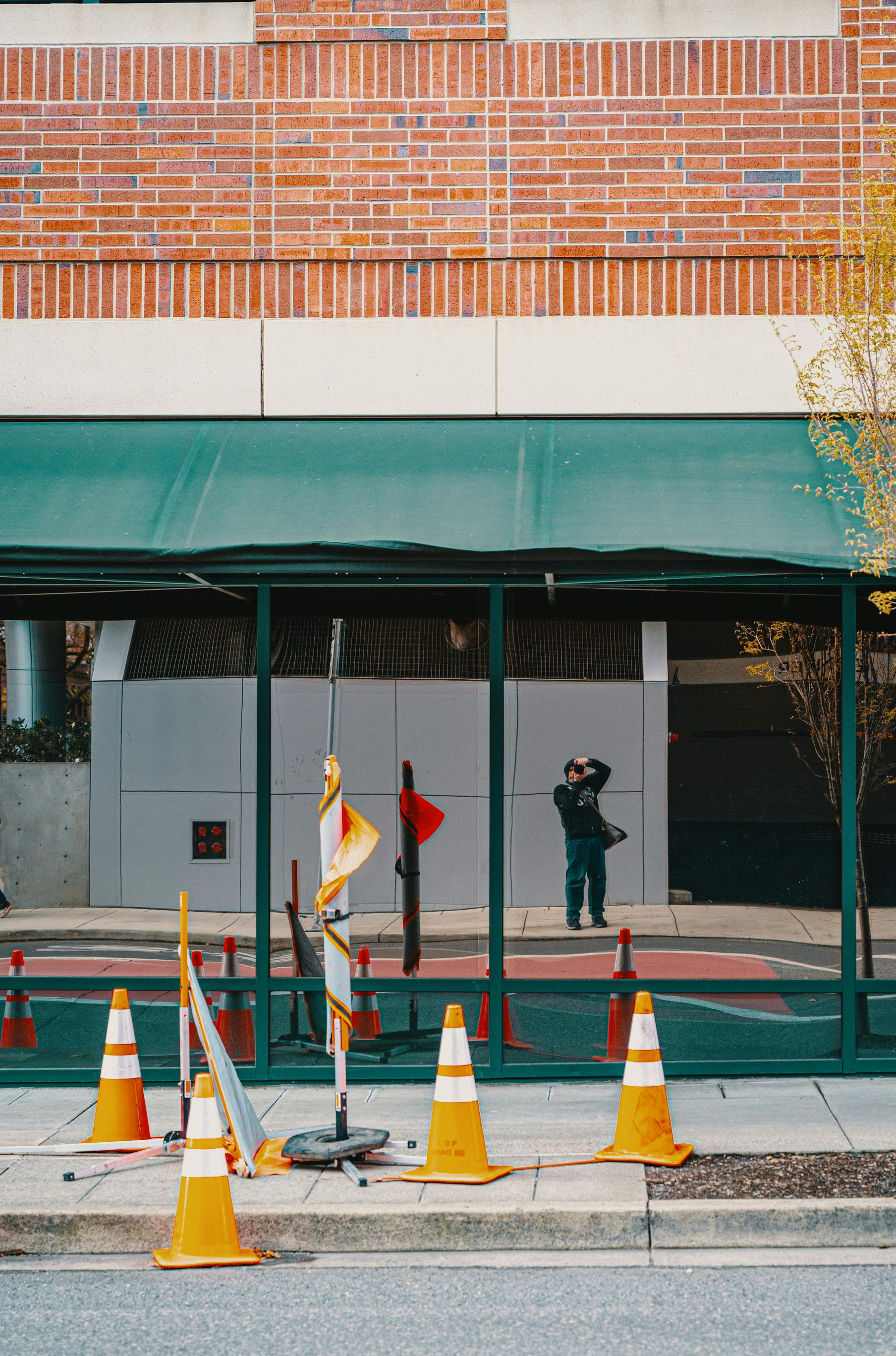 Construction cones and barriers in front of a building with green awning and reflective glass.
