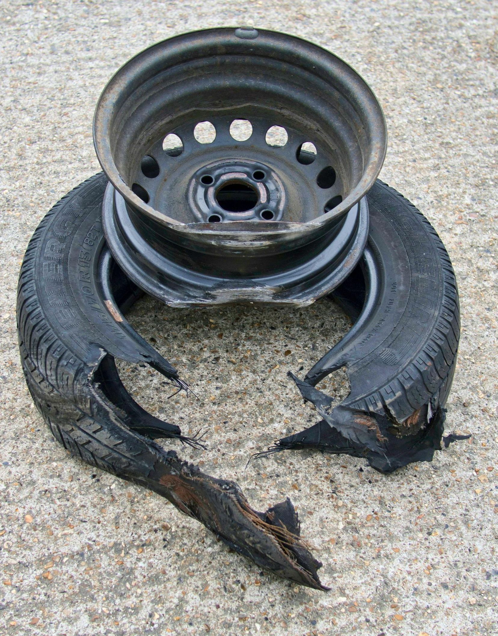 Damaged car tire and rim on pavement. The tire is torn apart, exposing the wheel.