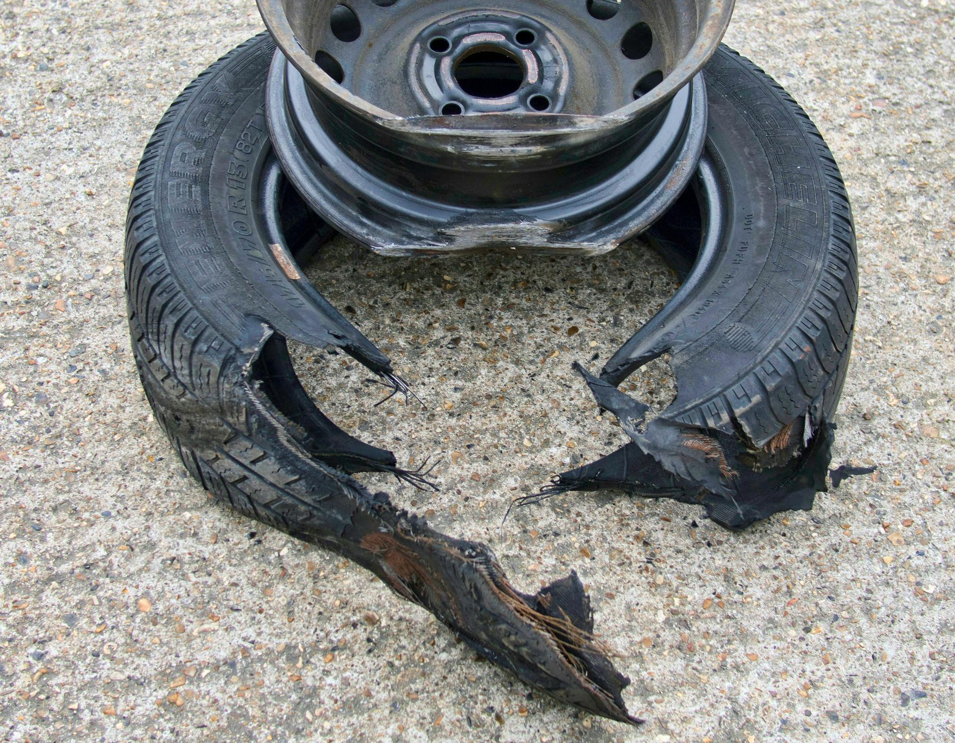 Damaged car tire with a split rim resting on concrete. Black rubber torn.
