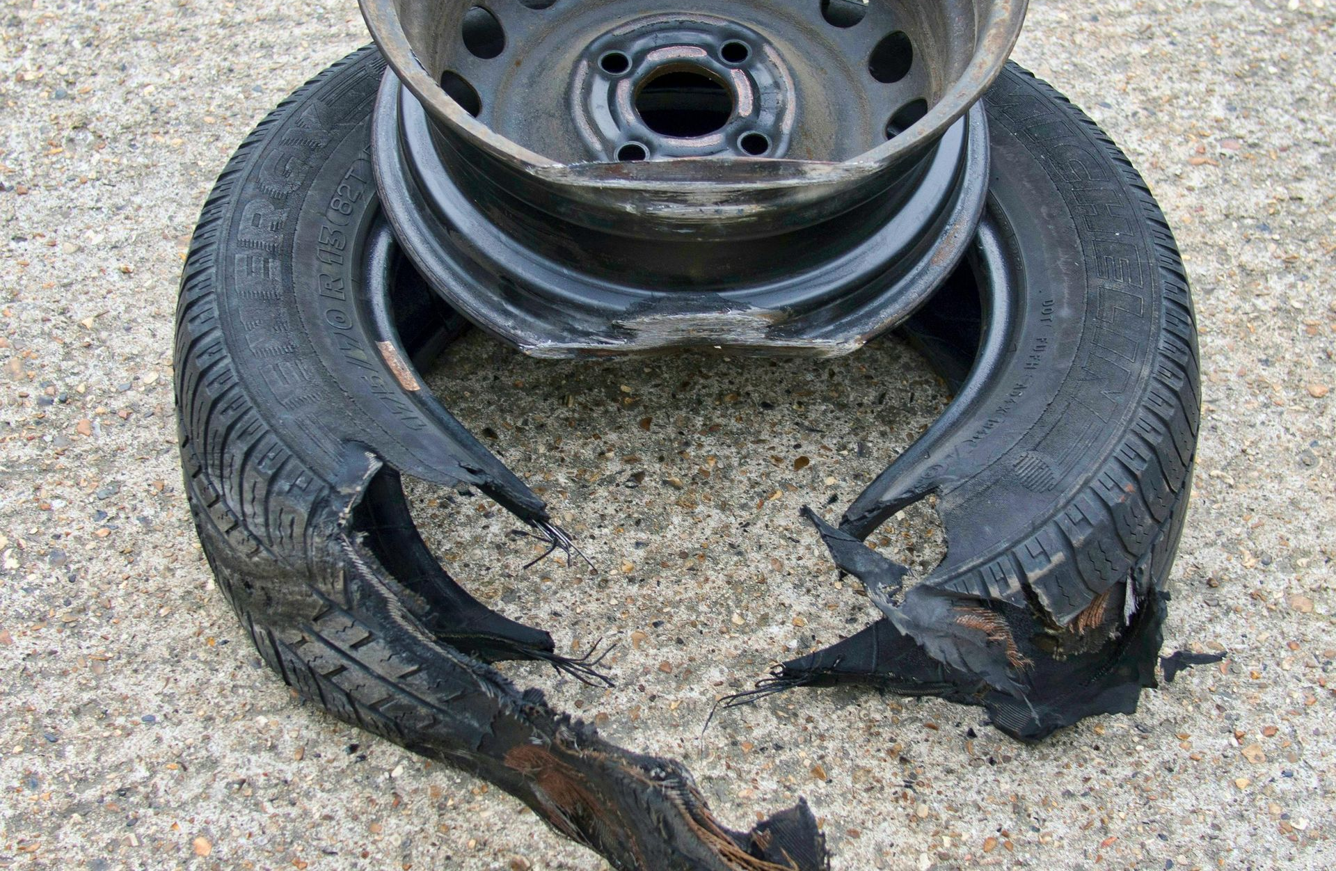 Damaged car tire with a split rim resting on concrete. Black rubber torn.