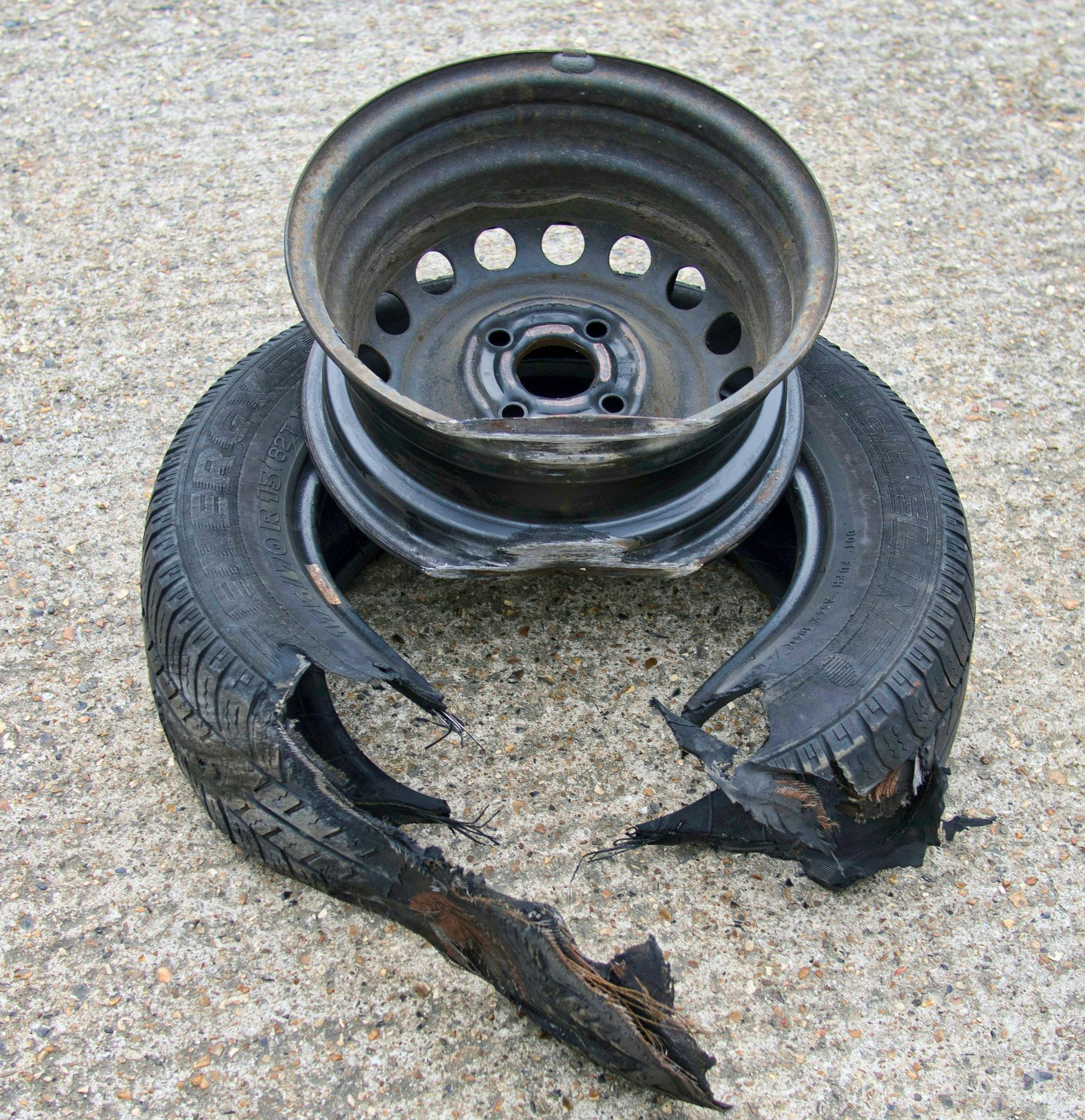 Damaged car tire with a split rim resting on concrete. Black rubber torn.