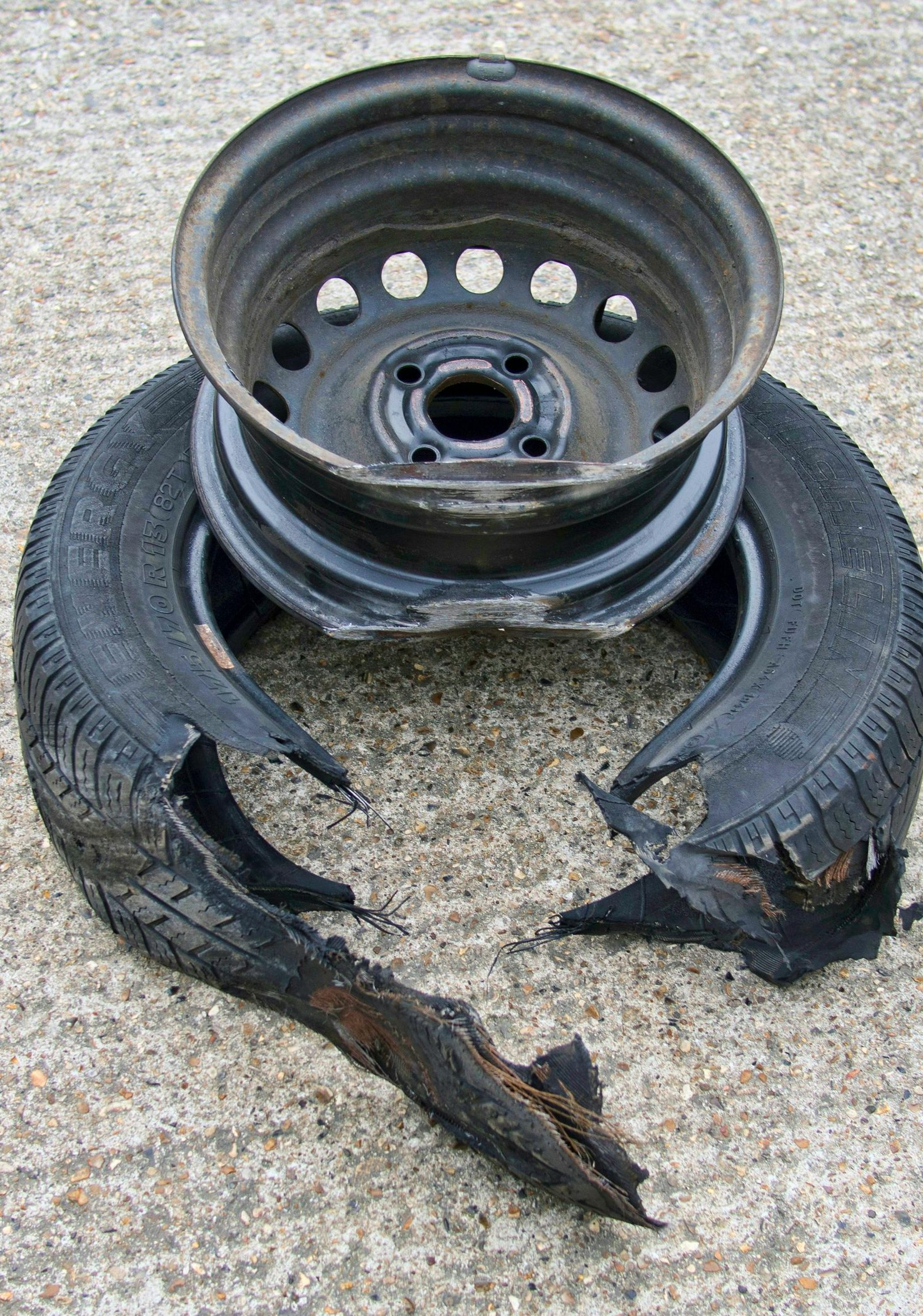 Damaged car tire and metal wheel on a concrete surface. Tire is split with detached pieces, wheel is dark.
