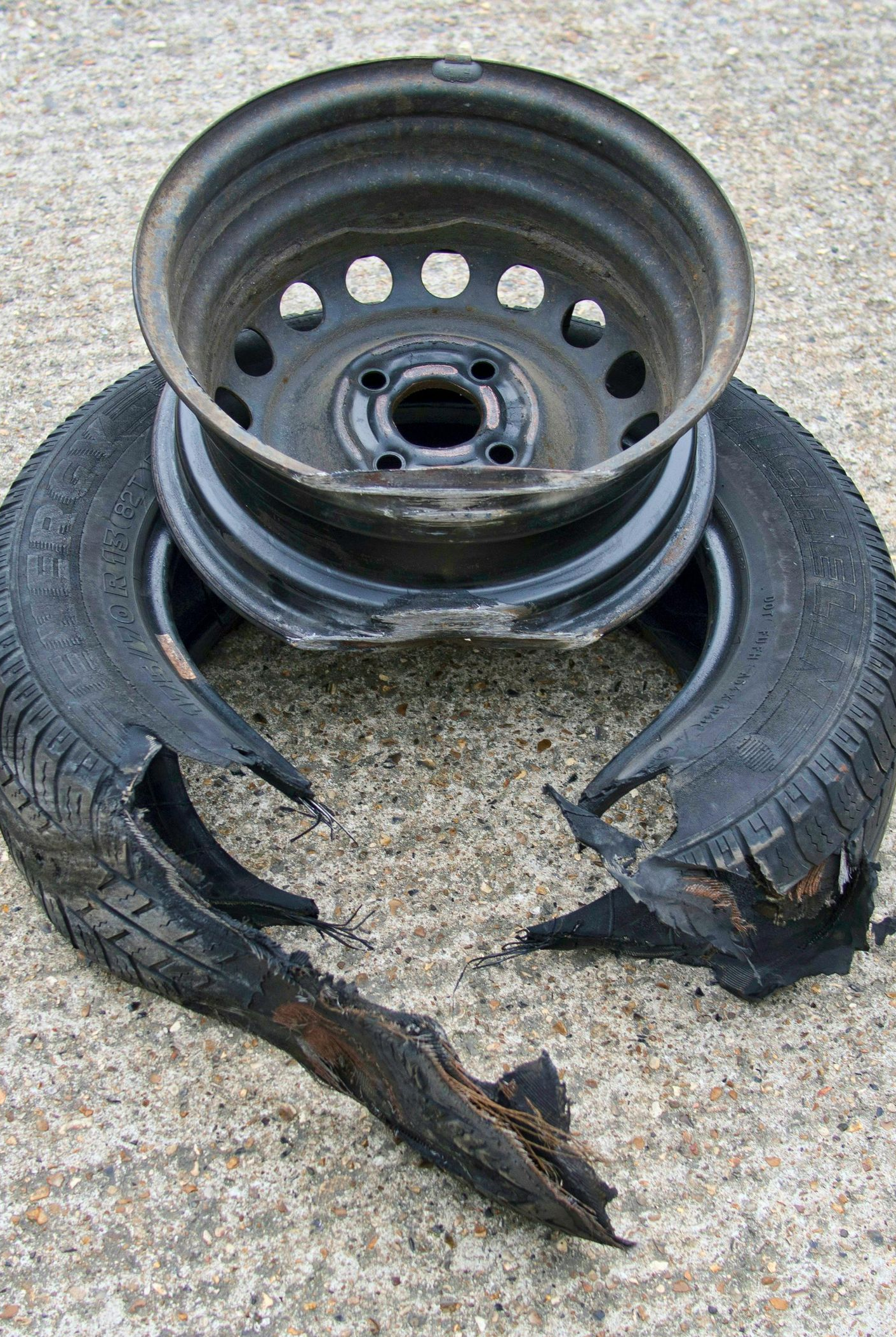 Damaged car tire and metal wheel on a concrete surface. Tire is split with detached pieces, wheel is dark.