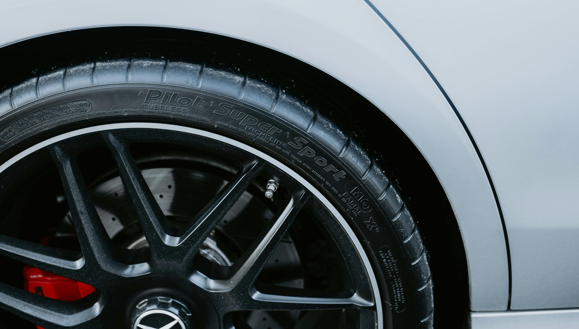 Black car tire and rim with red brake calipers, set against a grey fender.