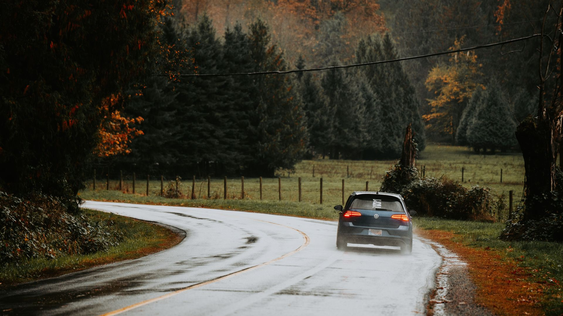 Car on a wet winding road through a dark forest in autumn