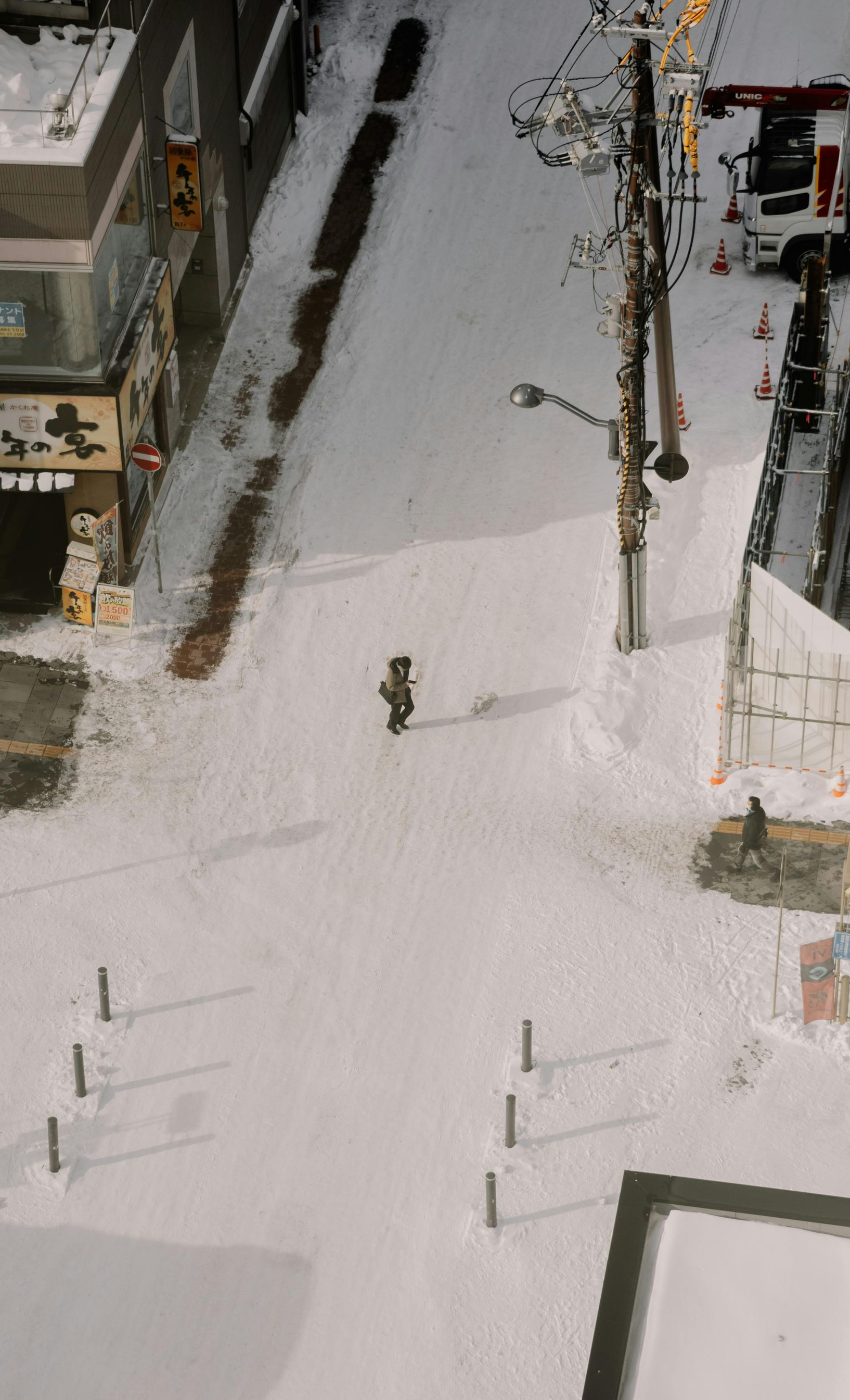 Snowy street scene, a person walking down a path through deep snow. Buildings and a utility pole line the street.