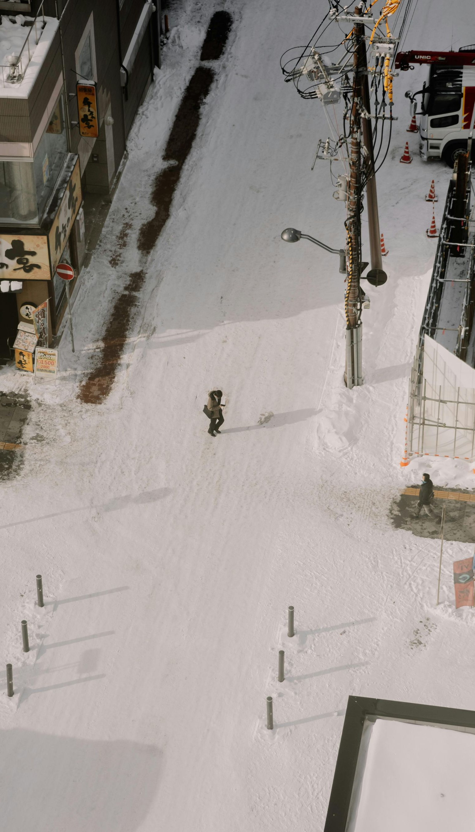 Snowy street scene, a person walking down a path through deep snow. Buildings and a utility pole line the street.