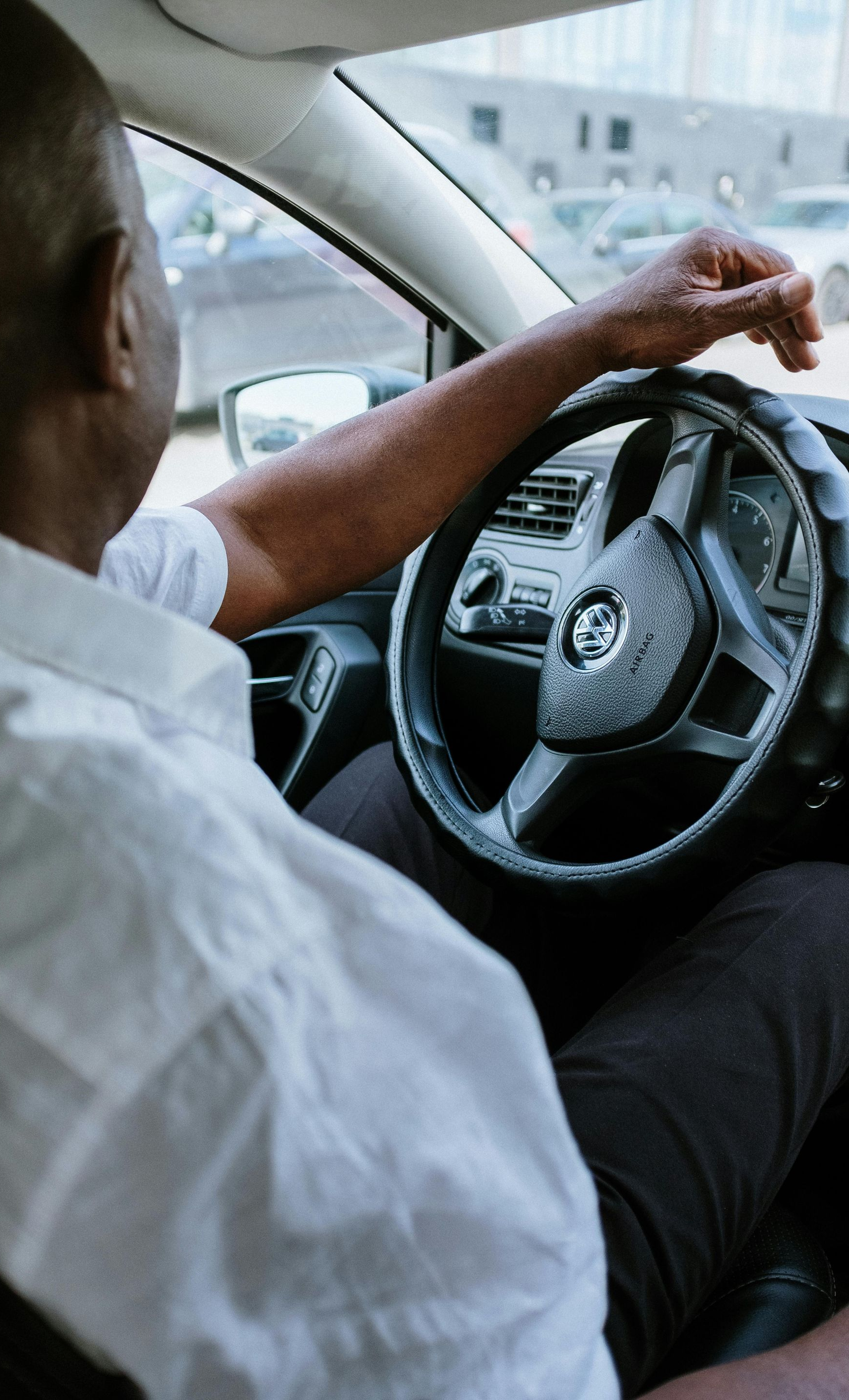 Driver sitting in a car, reaching toward the rearview mirror.