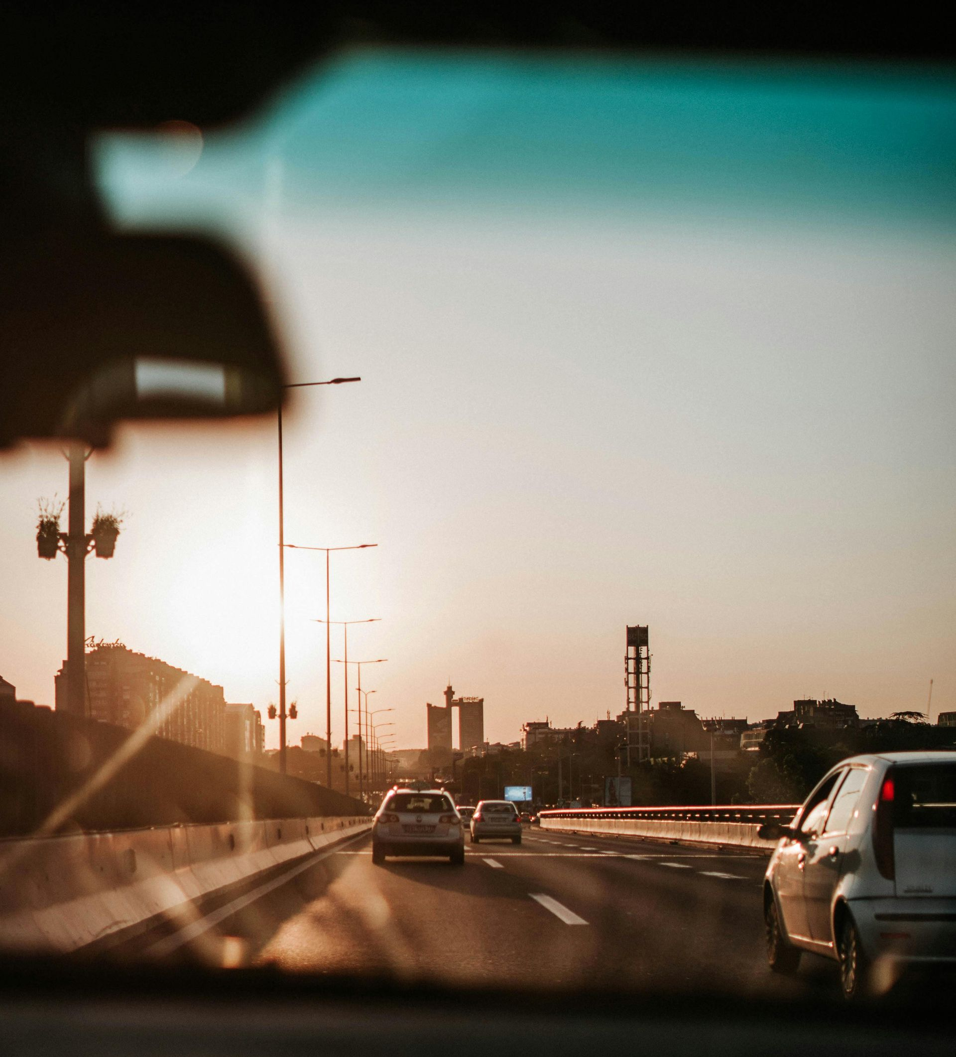 Cars driving on a highway at sunset, with a city skyline in the distance.
