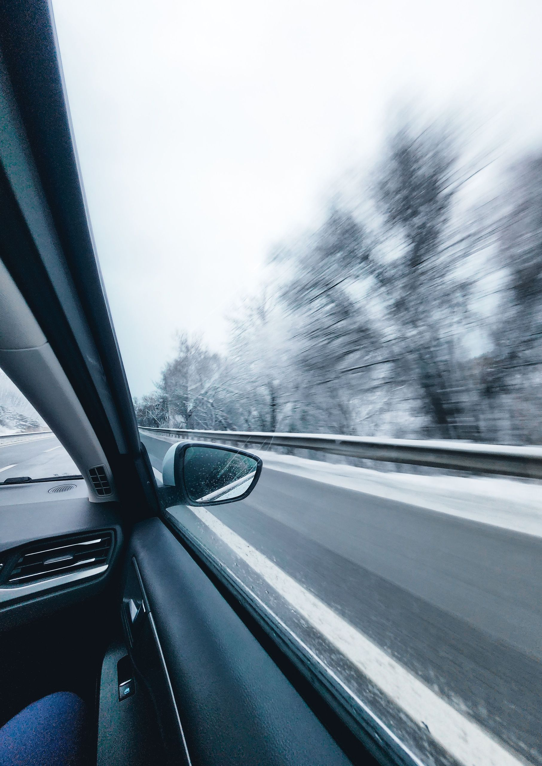 View from a car driving on a snowy highway, with blurred trees and guardrails passing by
