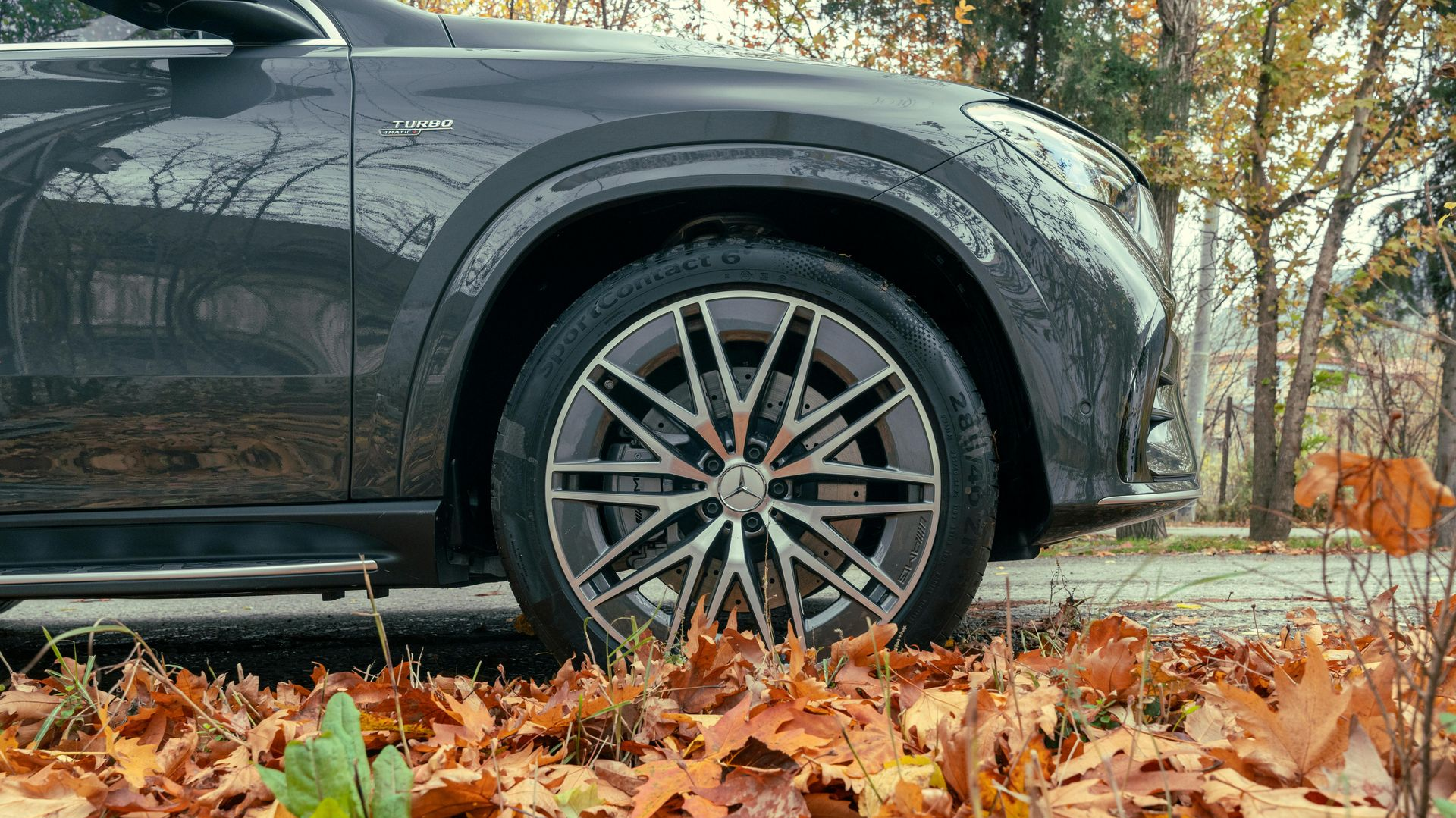 Gray car wheel on a road covered in autumn leaves.