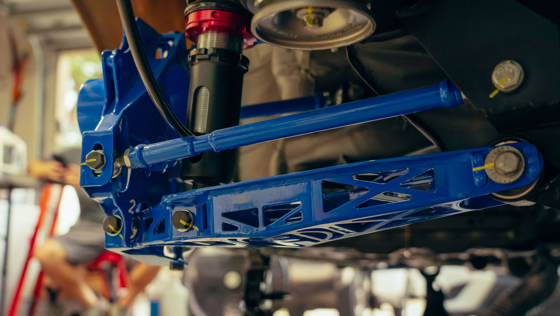 Blue car suspension and undercarriage components on a vehicle lift in a garage.