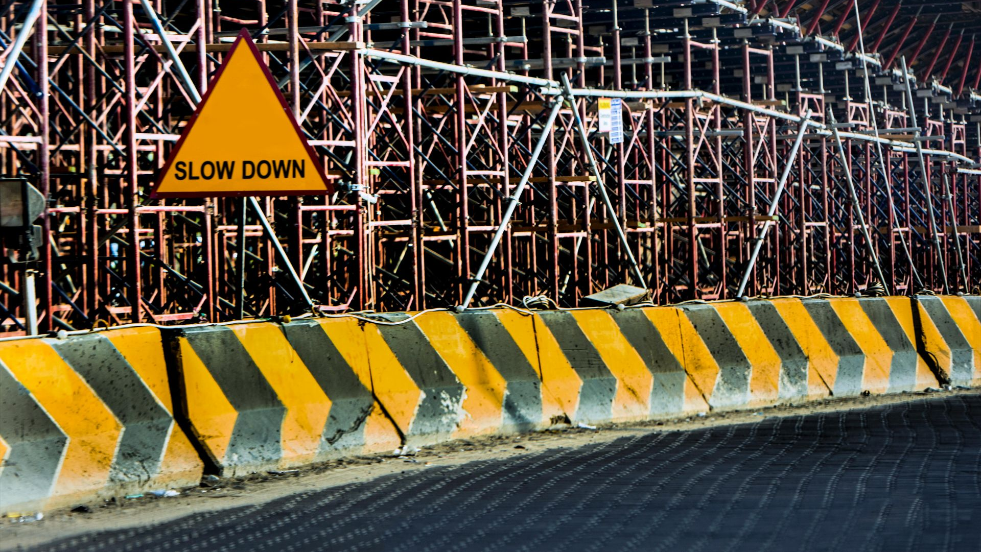 Road construction site with yellow-black barriers and a slow down sign under scaffolding