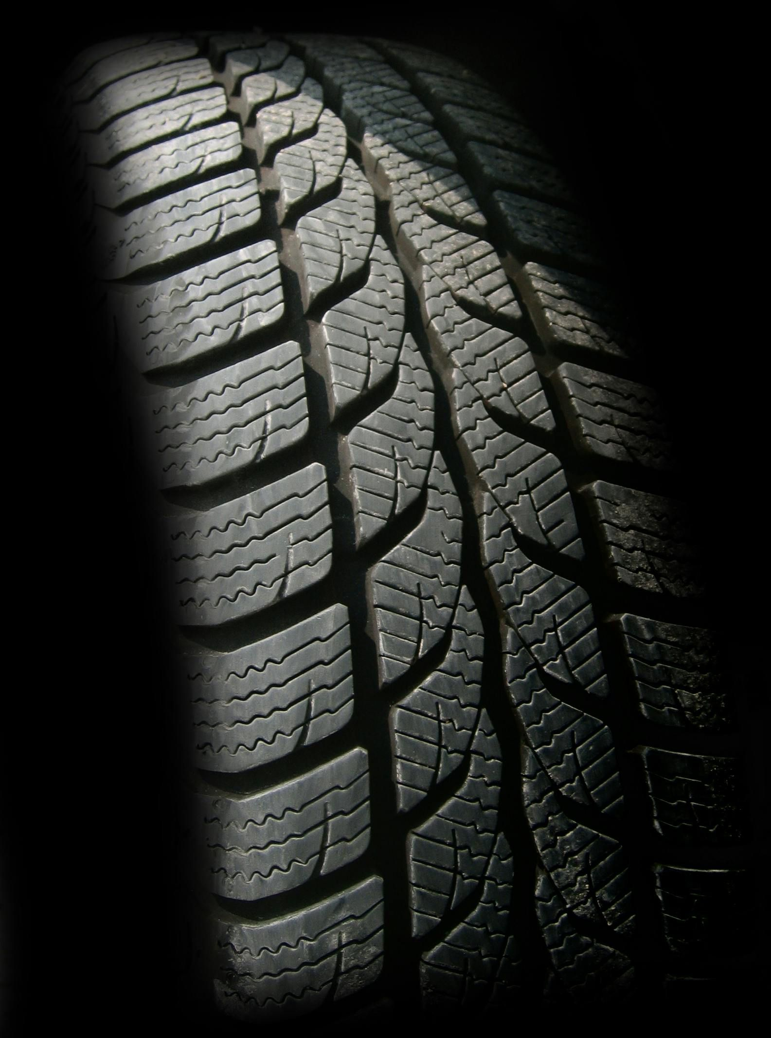 Close-up view of a car tire with a deep tread pattern, angled against a black background.