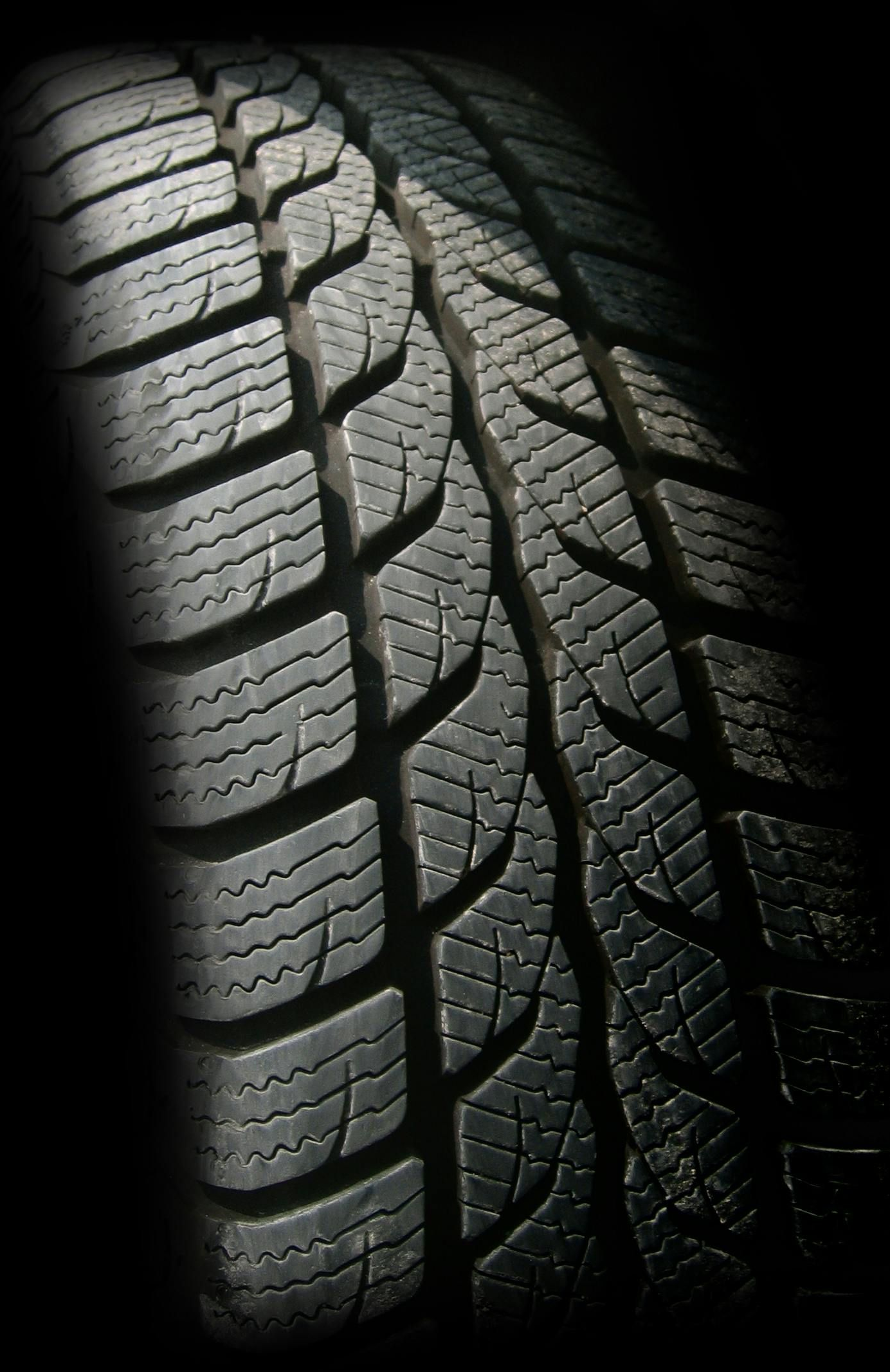 Close-up view of a car tire with a deep tread pattern, angled against a black background.