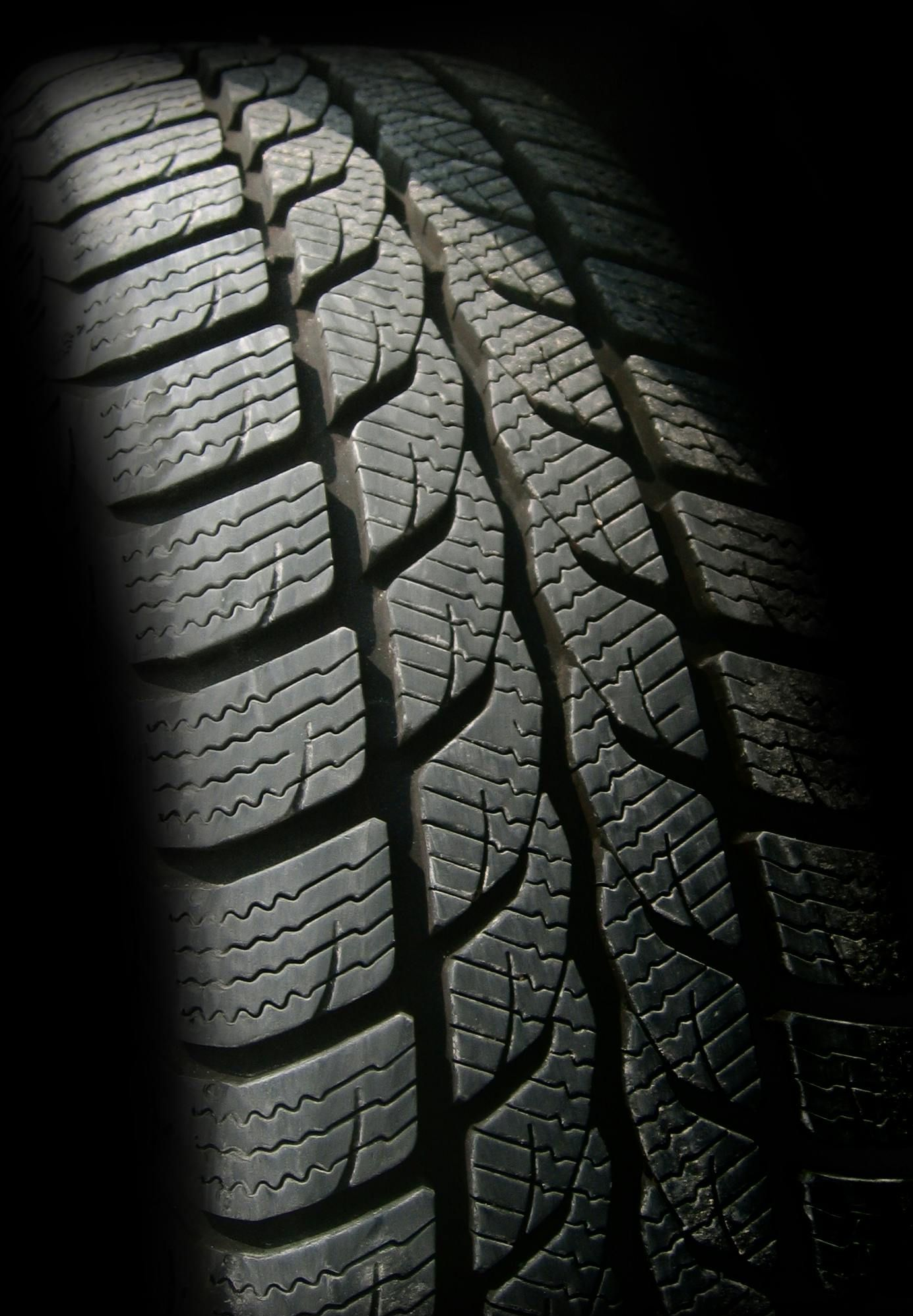 Close-up of a tire with a deeply grooved tread pattern, partially lit and set against a dark background.
