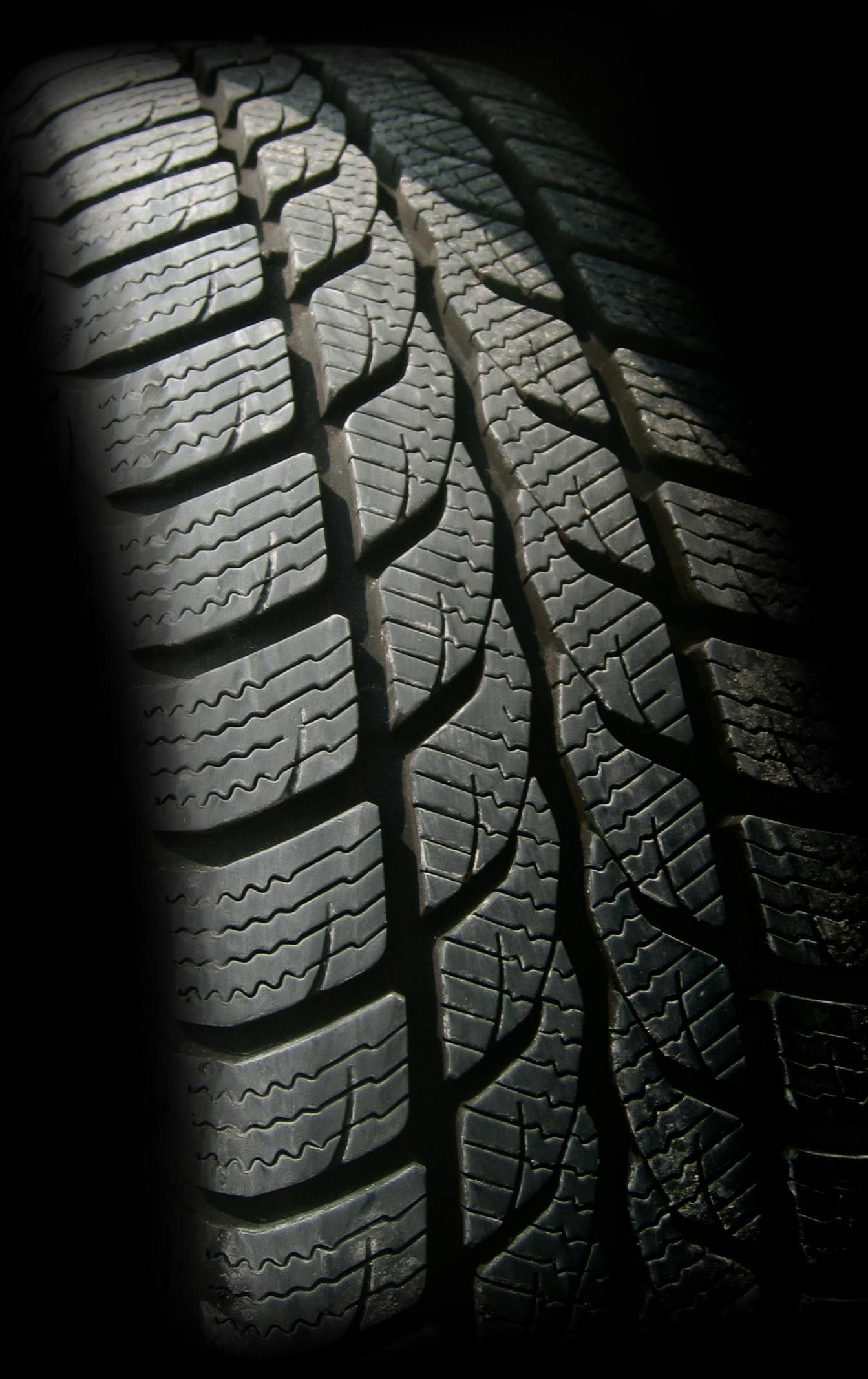 Close-up view of a car tire with a deep tread pattern, angled against a black background.