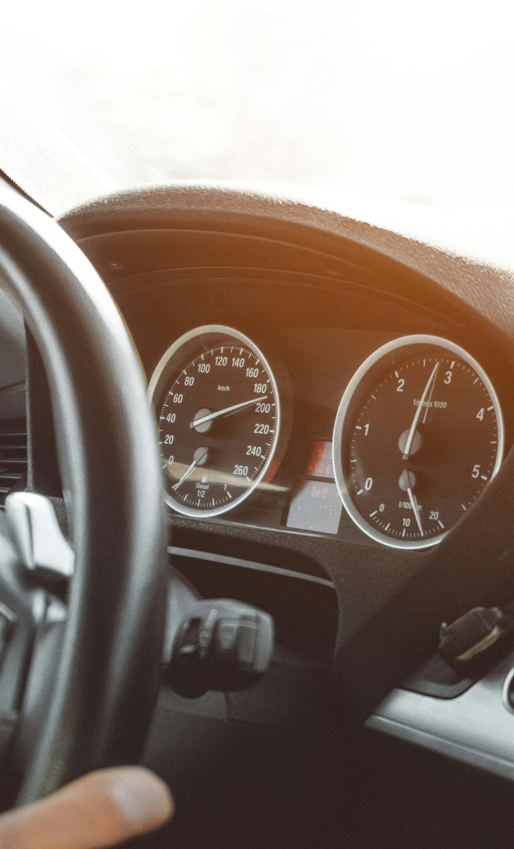 Dashboard of a car with a hand on the steering wheel, gauges visible. Sunlight shines.
