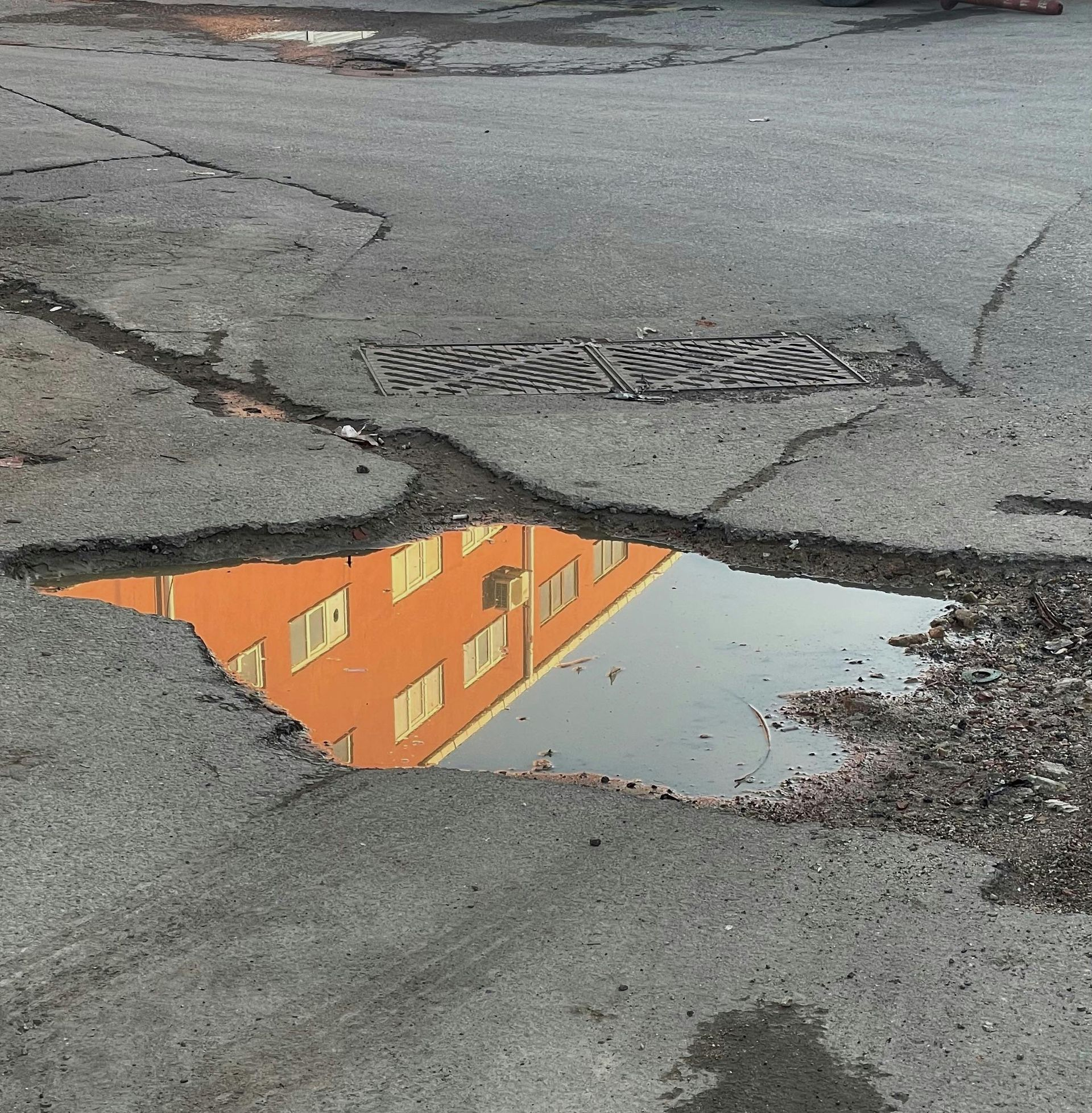 Puddle reflecting a bright orange building with windows on cracked asphalt.