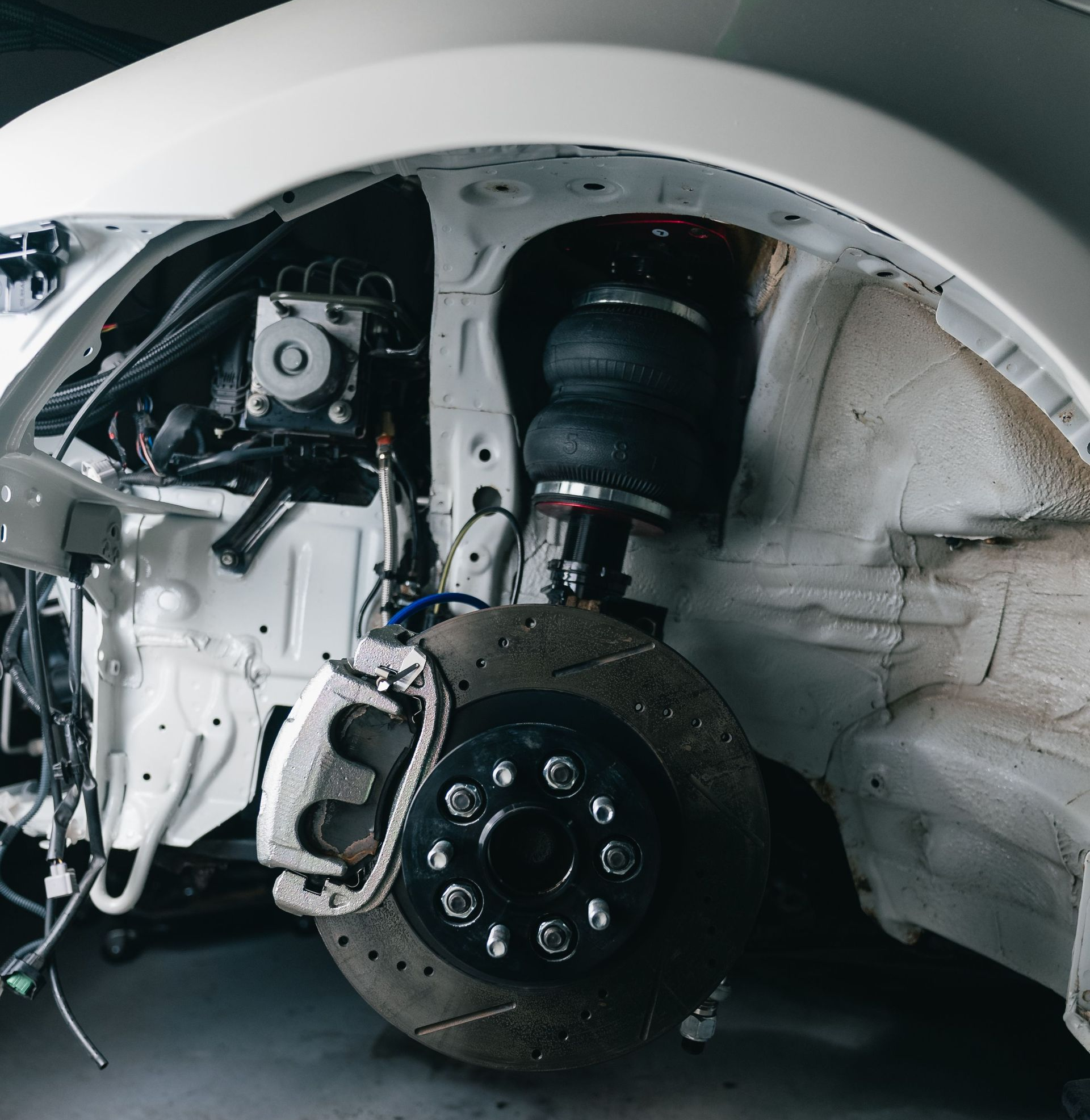 Car with front wheel removed, exposing brake and suspension inside a garage