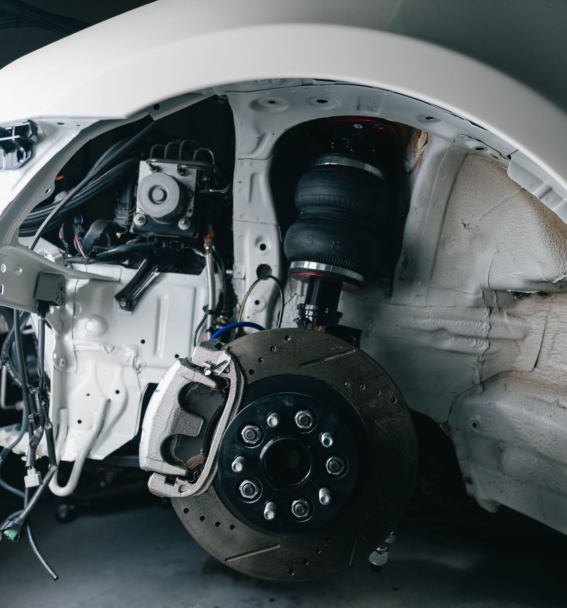 Car with front wheel removed, exposing brake and suspension inside a garage