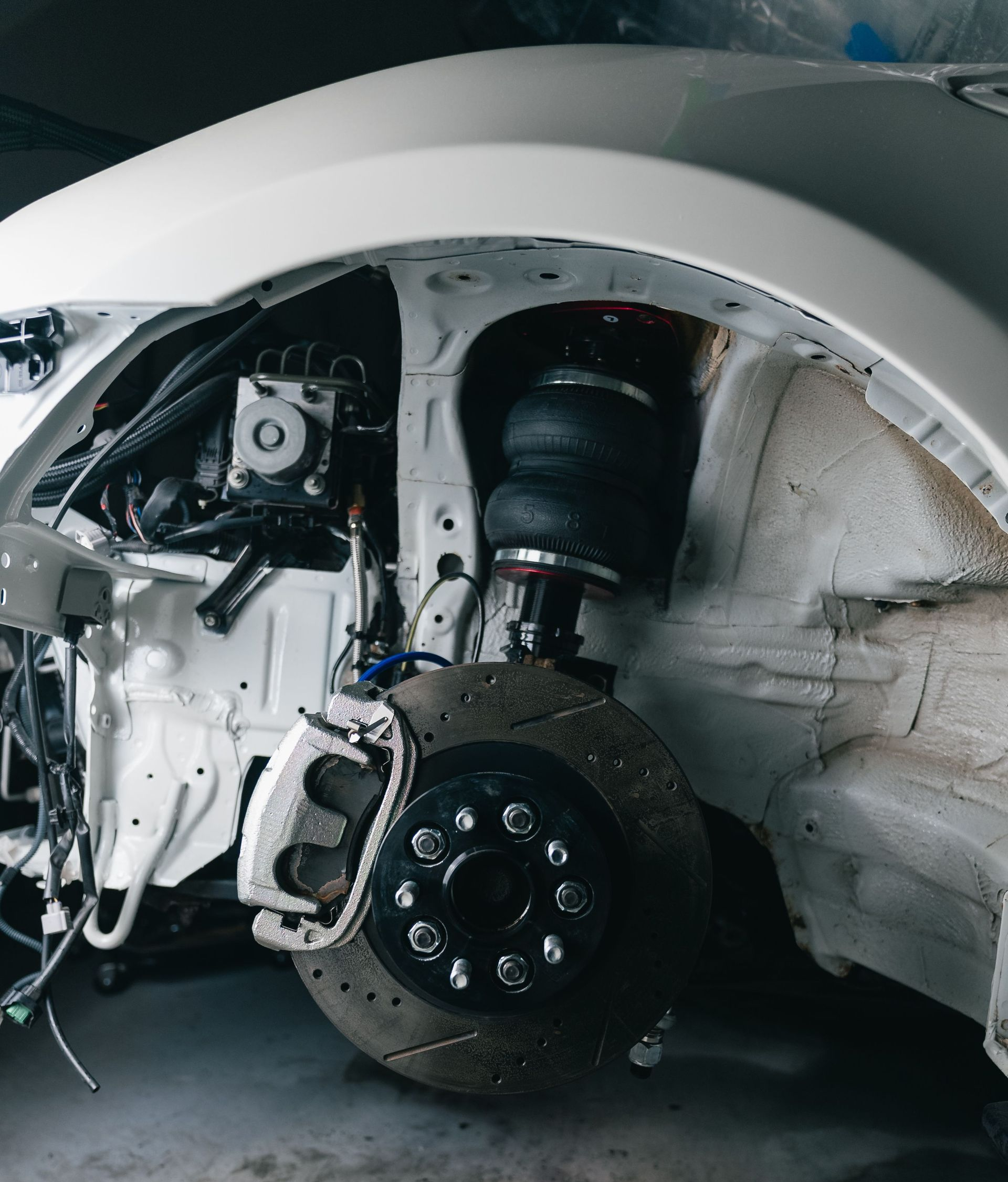 Car with front wheel removed, exposing brake and suspension inside a garage