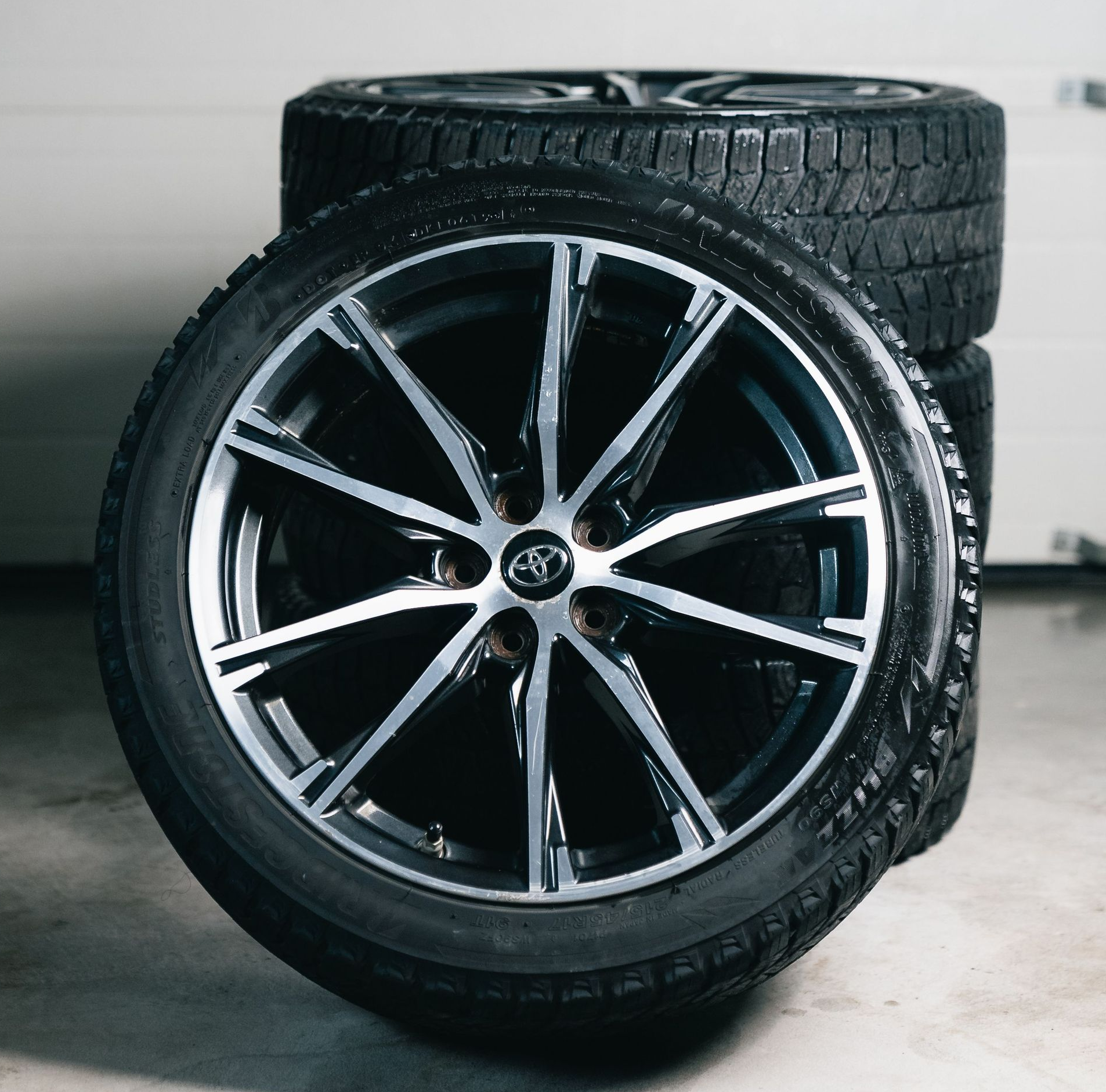 Two black car tires, one upright with alloy rim, in a garage setting