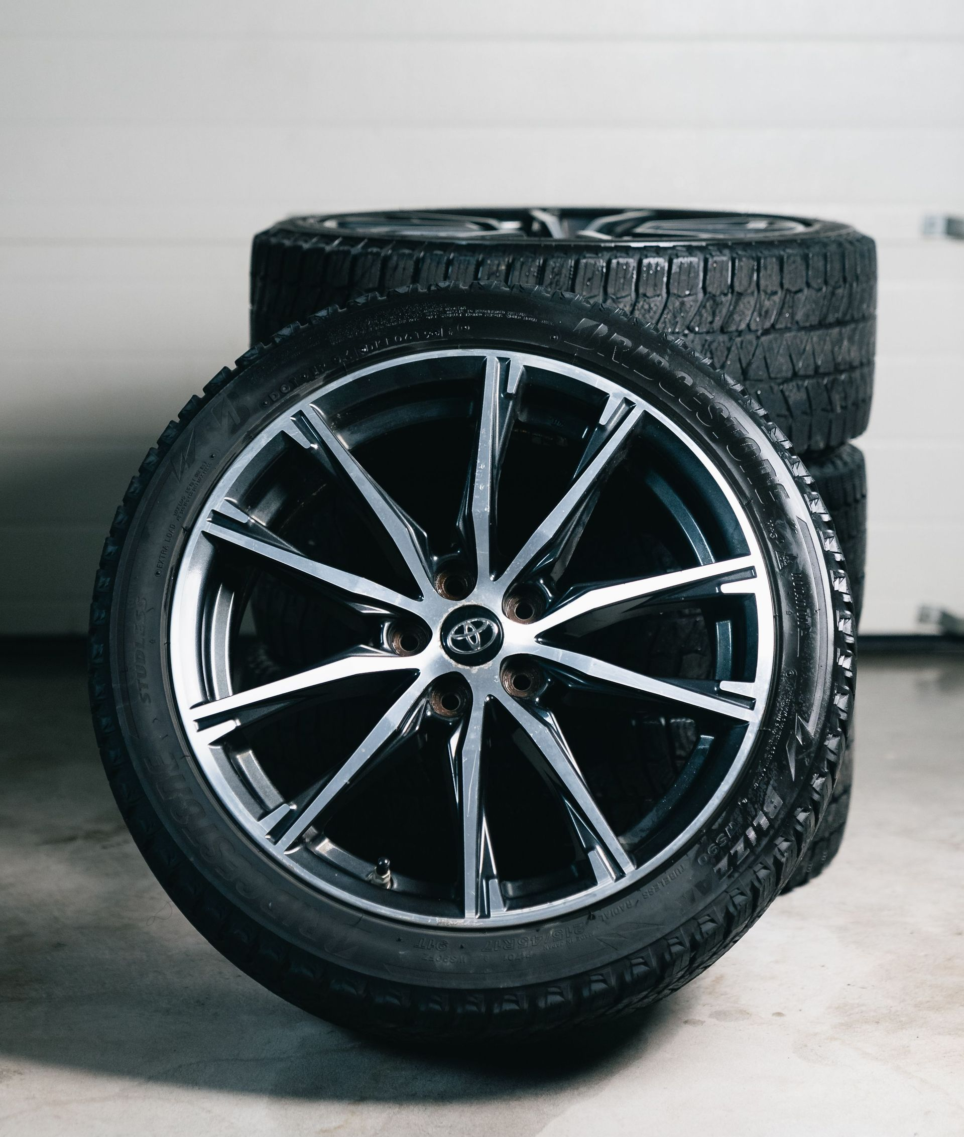 Two black car tires, one upright with alloy rim, in a garage setting
