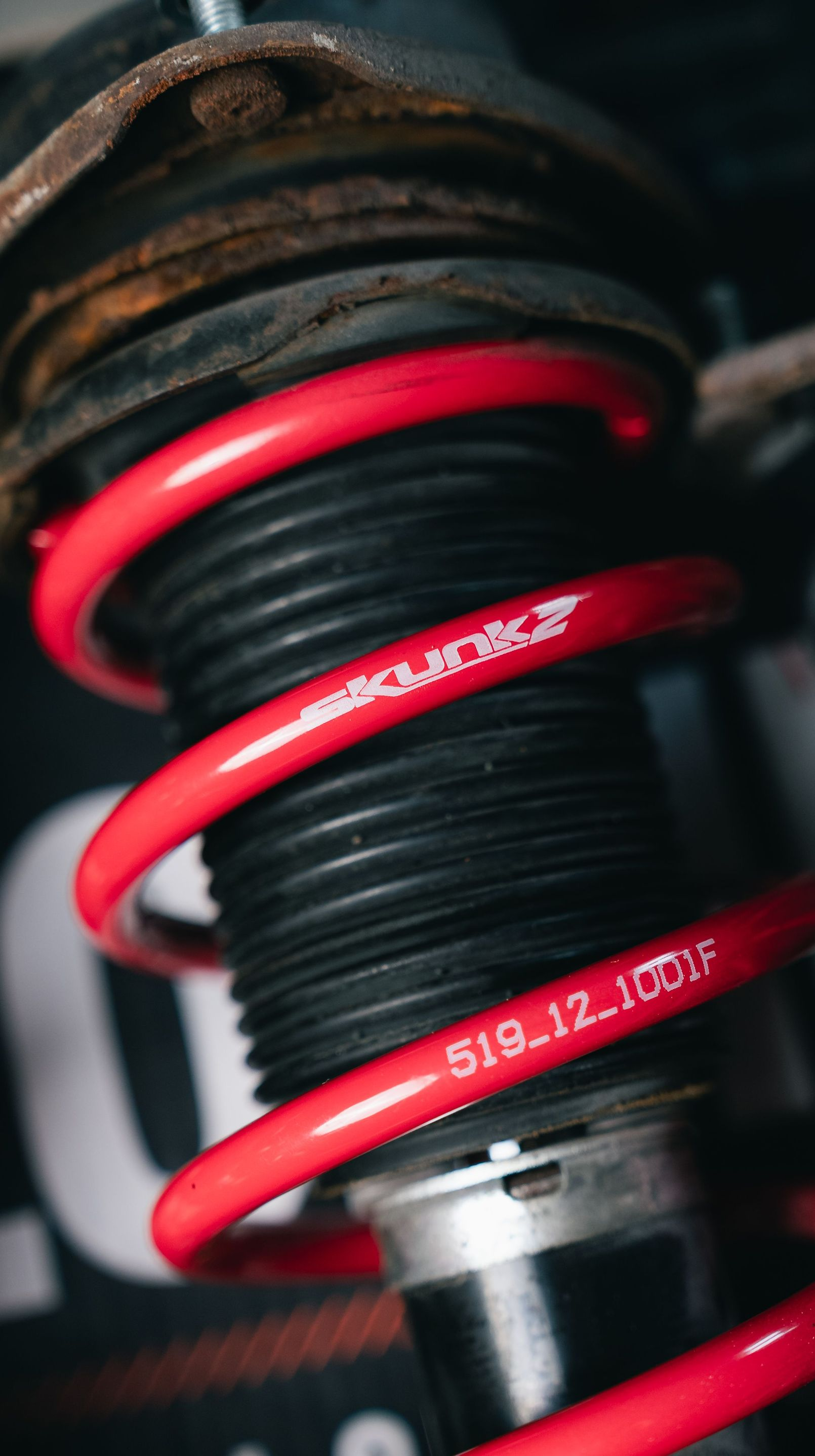 Close-up of a red coilover spring and shock absorber on a vehicle suspension.