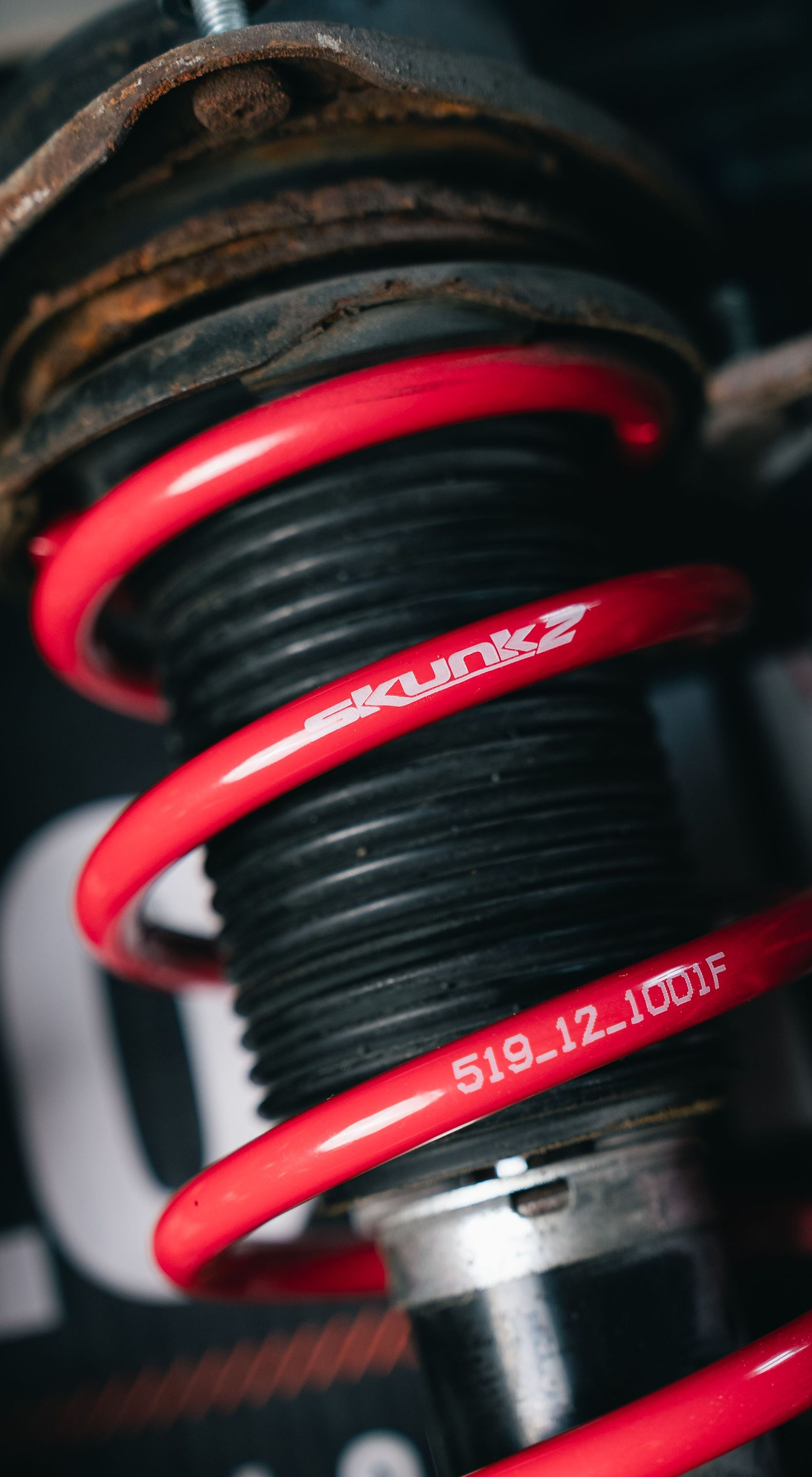 Close-up of a red coilover spring and shock absorber on a vehicle suspension.