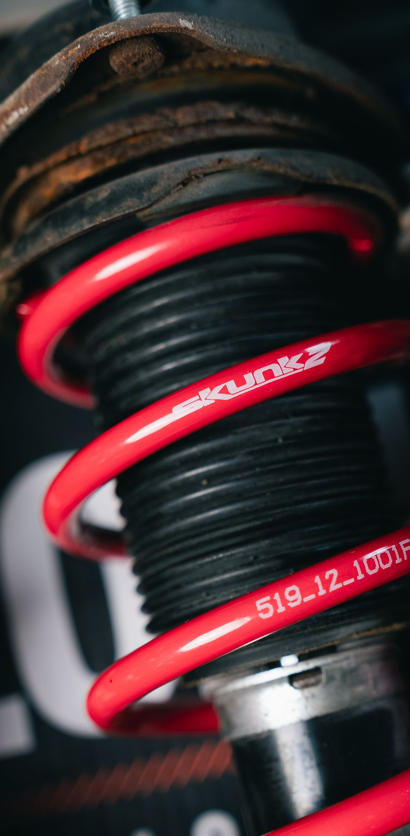 Close-up of a red coilover spring and shock absorber on a vehicle suspension.