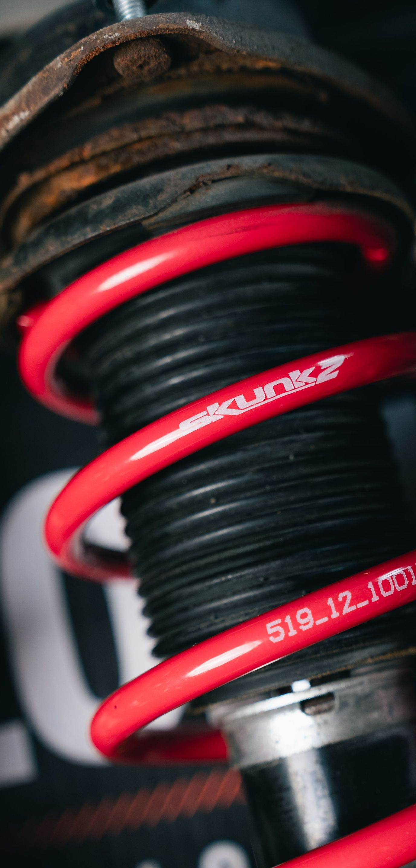 Close-up of a red coilover spring and shock absorber on a vehicle suspension.