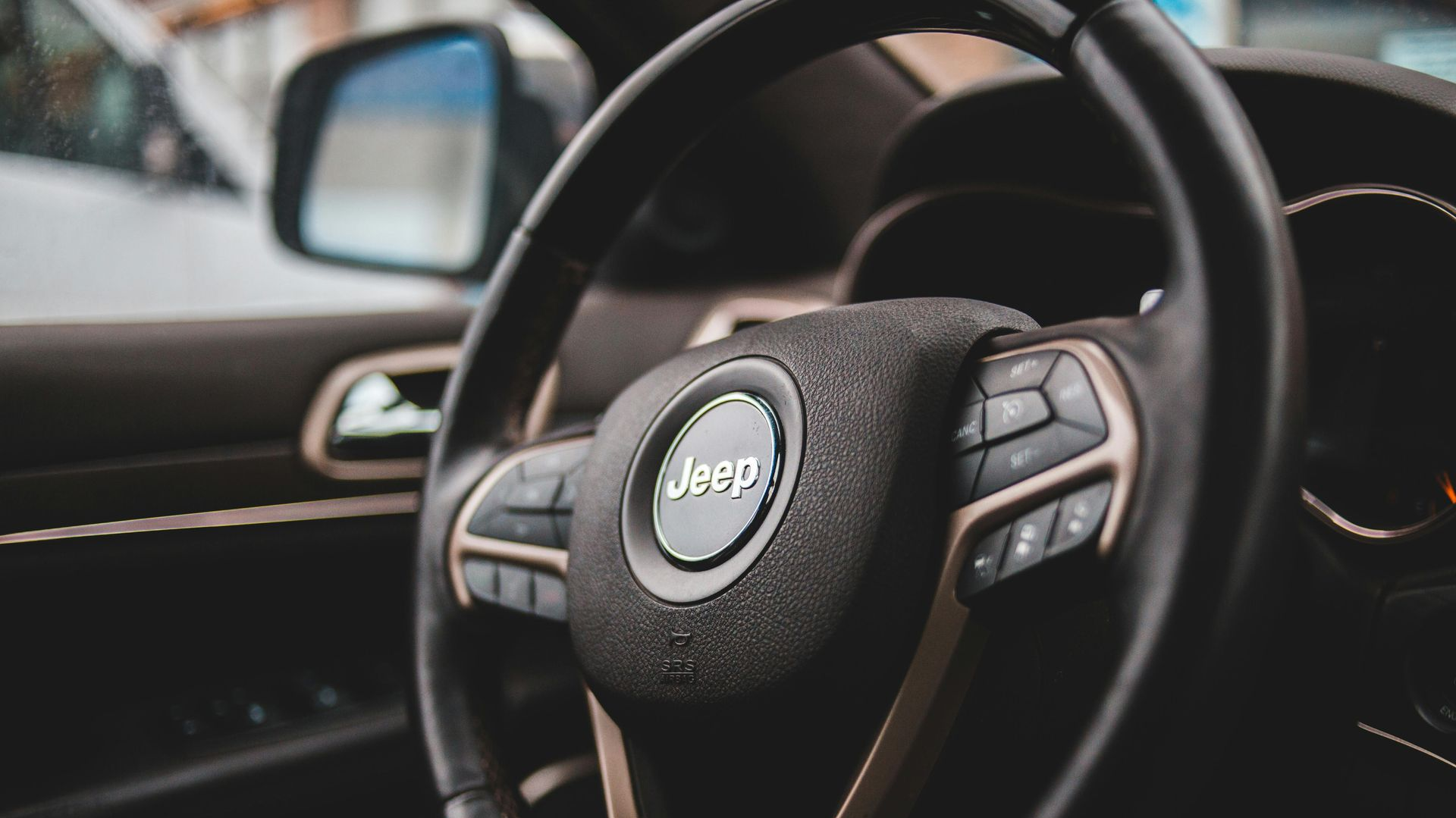 Jeep steering wheel with controls; dark leather and metallic accents inside a vehicle.