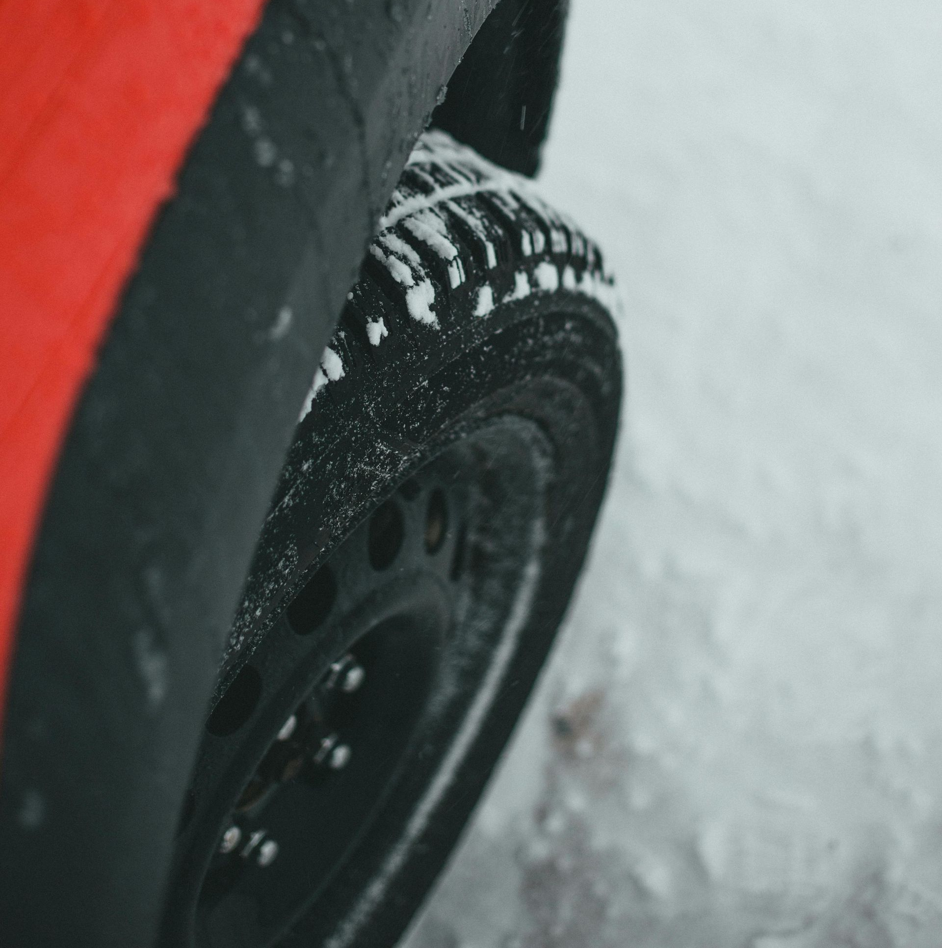 Red car tire covered in snow on a winter road.