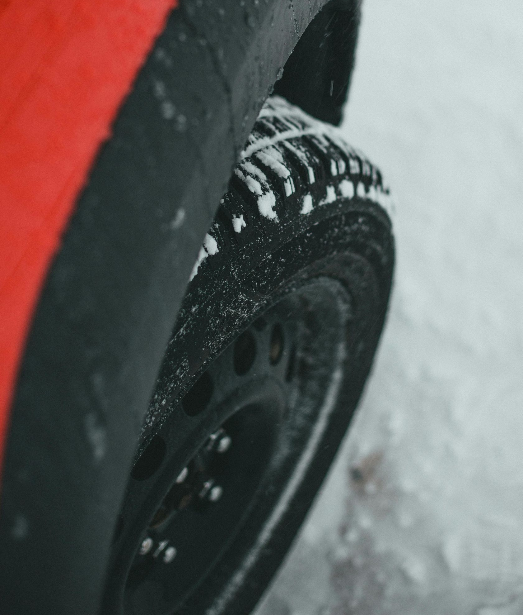 Red car tire covered in snow on a winter road.