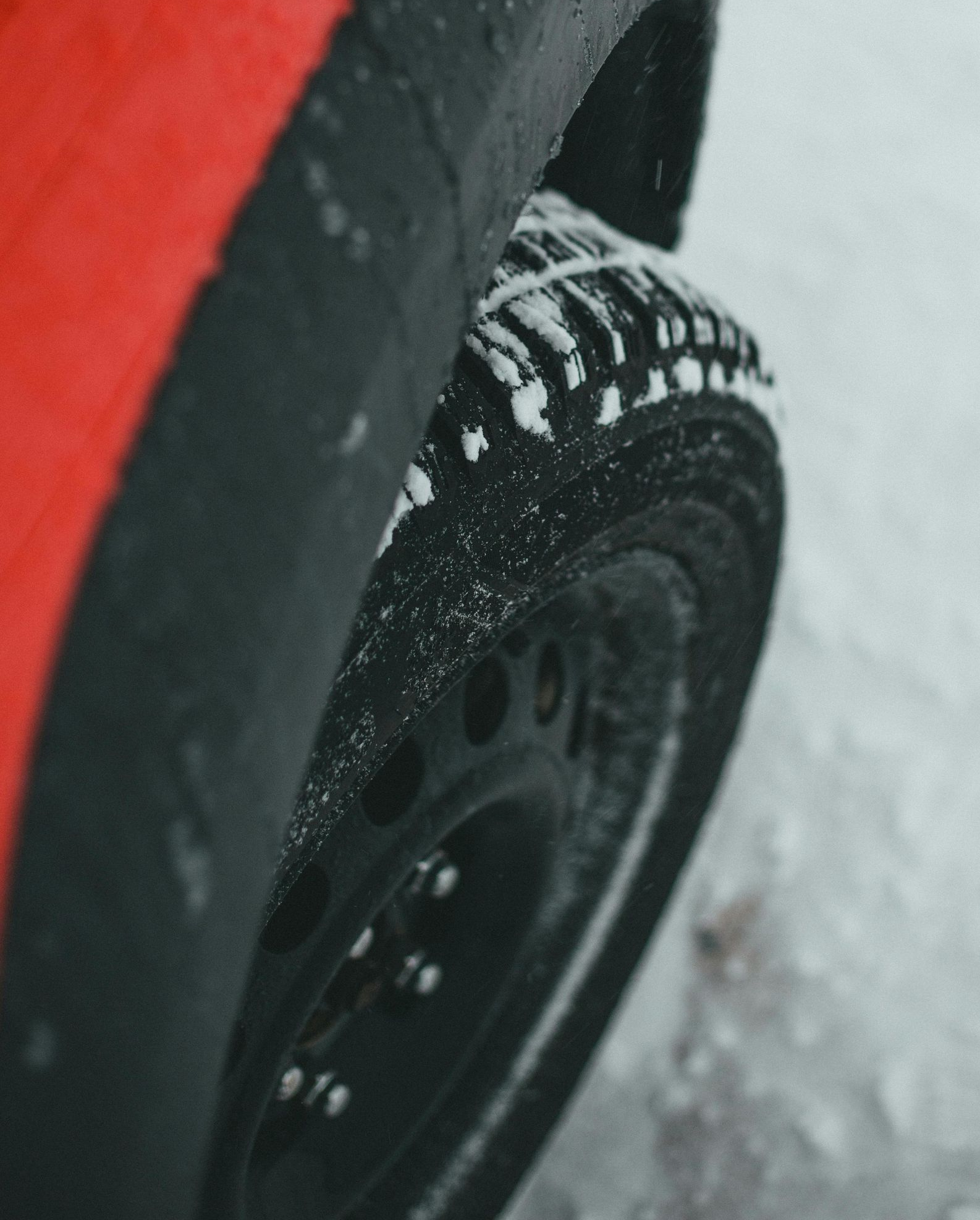 Red car tire covered in snow on a winter road.