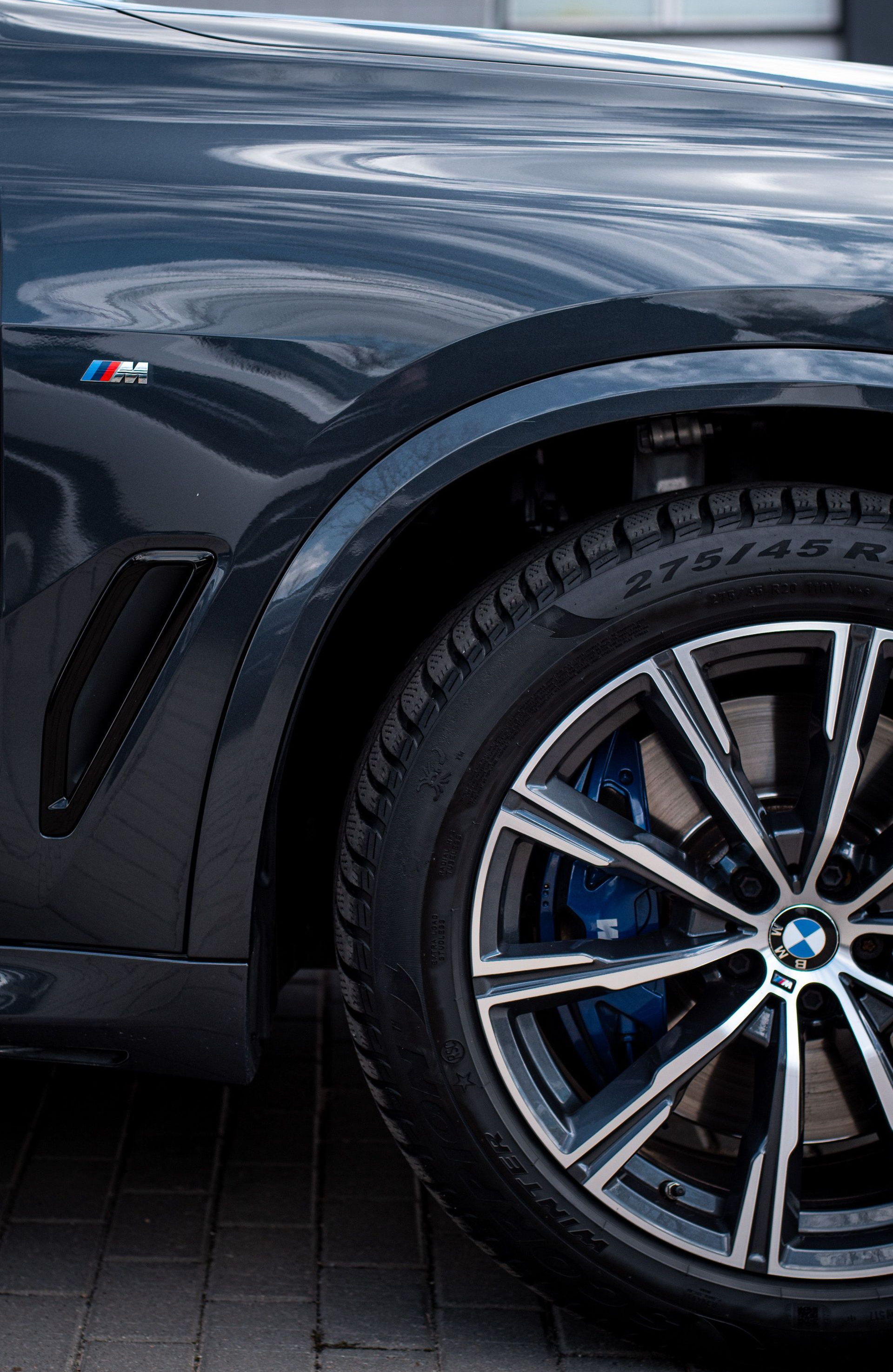 Close-up of a dark blue sports car’s front wheel and fender with M badge