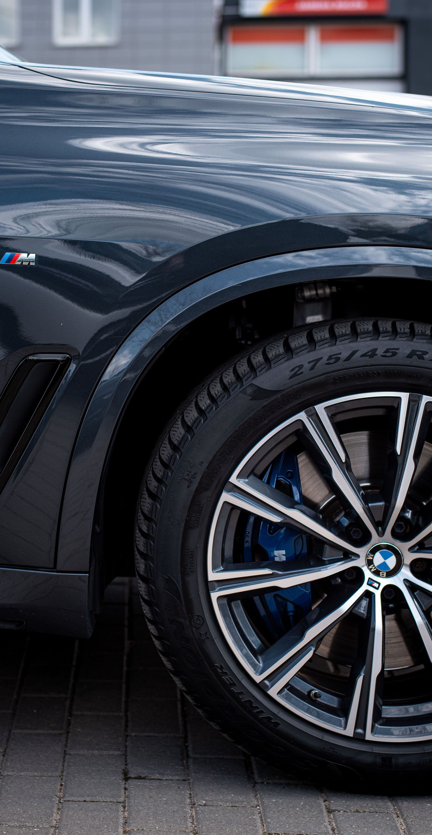 Close-up of a dark blue sports car’s front wheel and fender with M badge