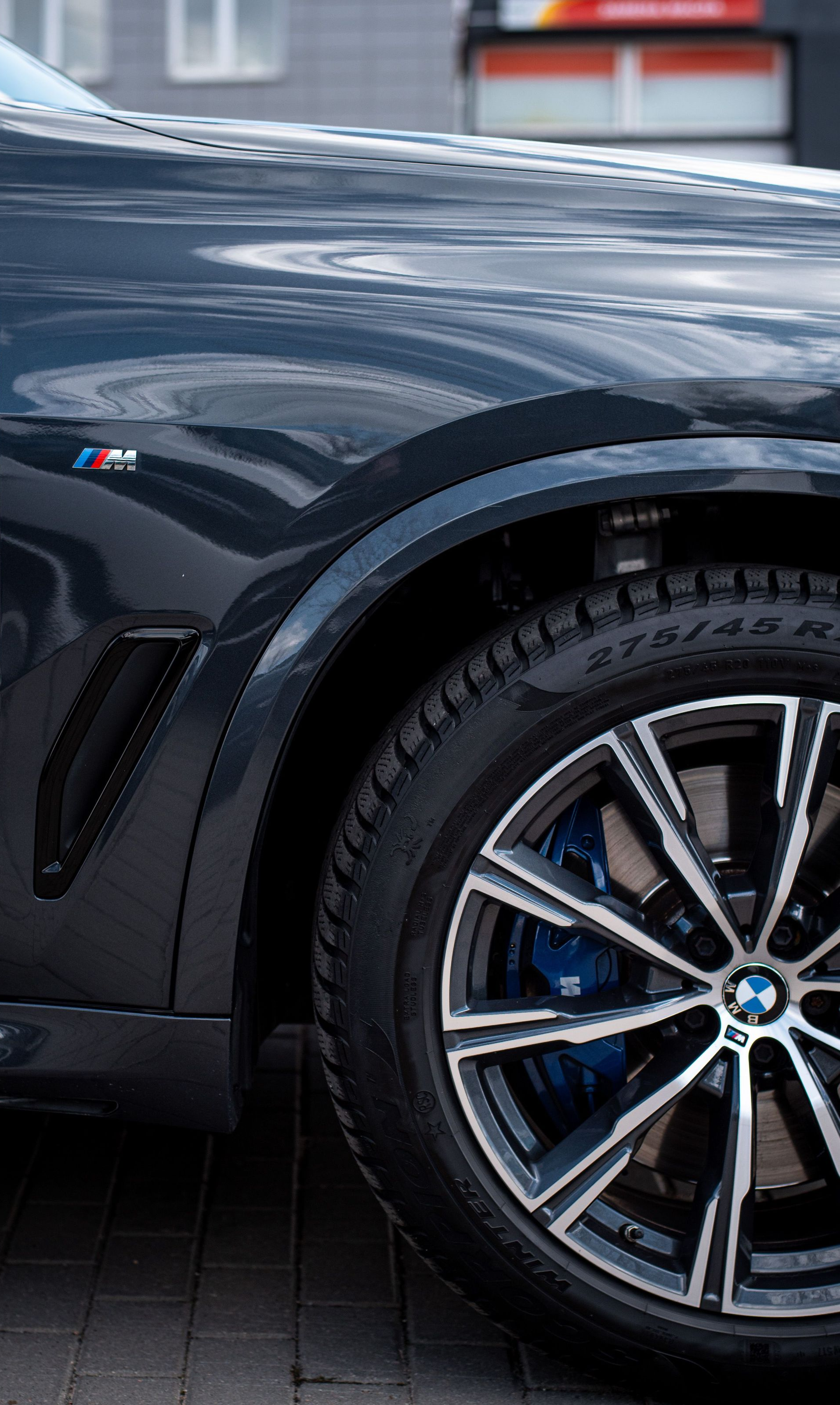 Close-up of a dark blue sports car’s front wheel and fender with M badge