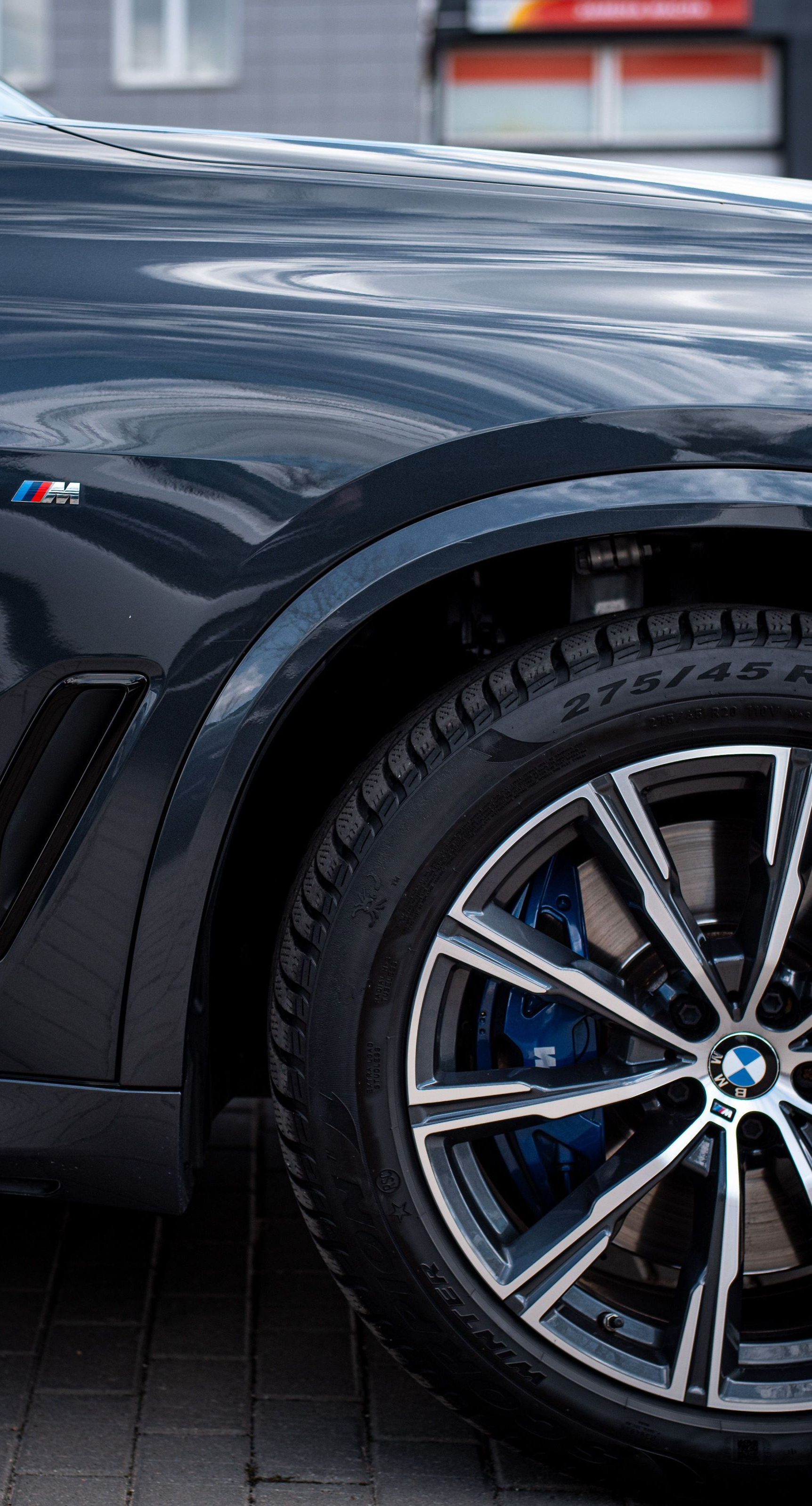 Close-up of a dark blue sports car’s front wheel and fender with M badge