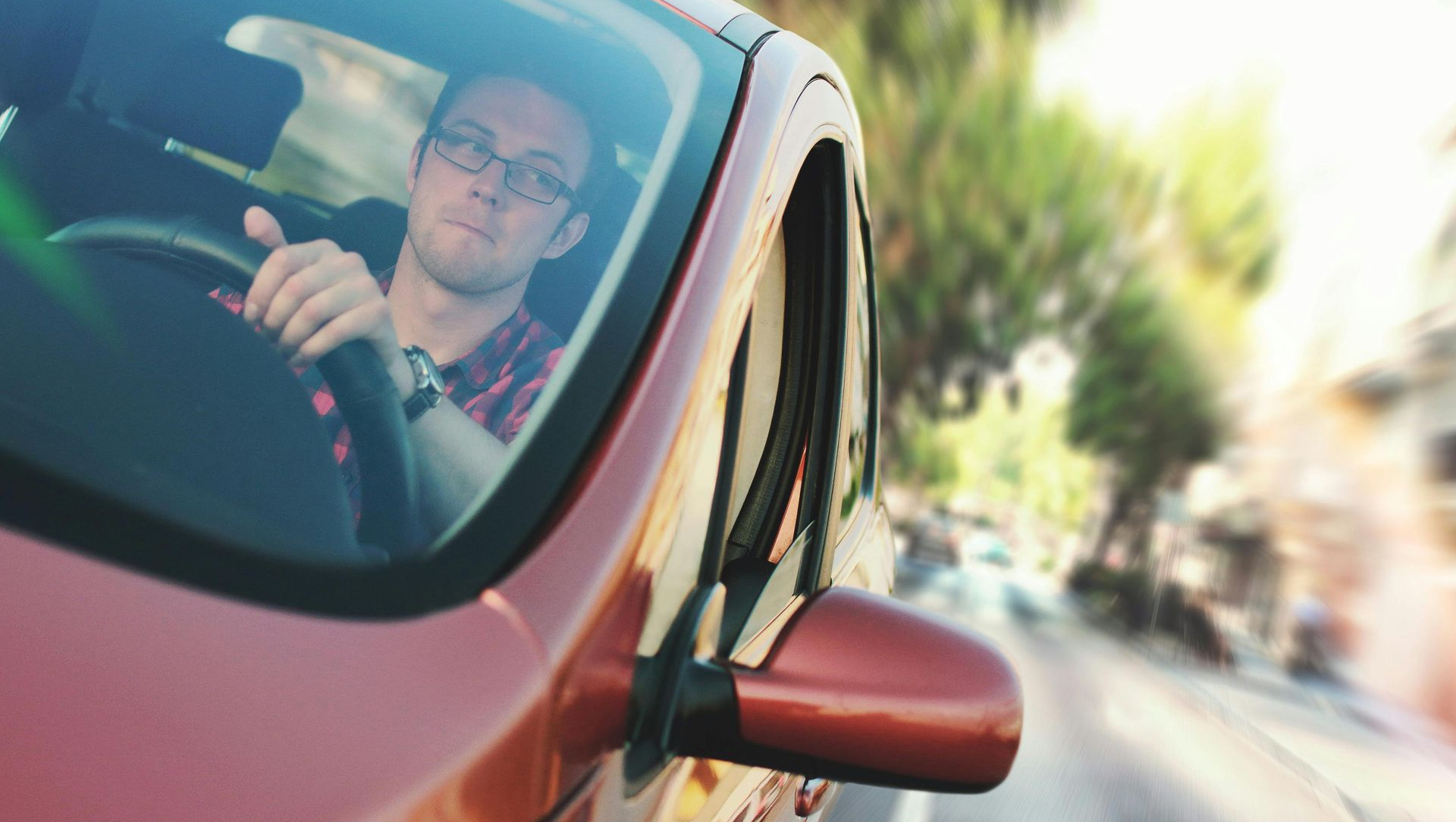 Man driving a red car, seen through the windshield with a blurred street in the background