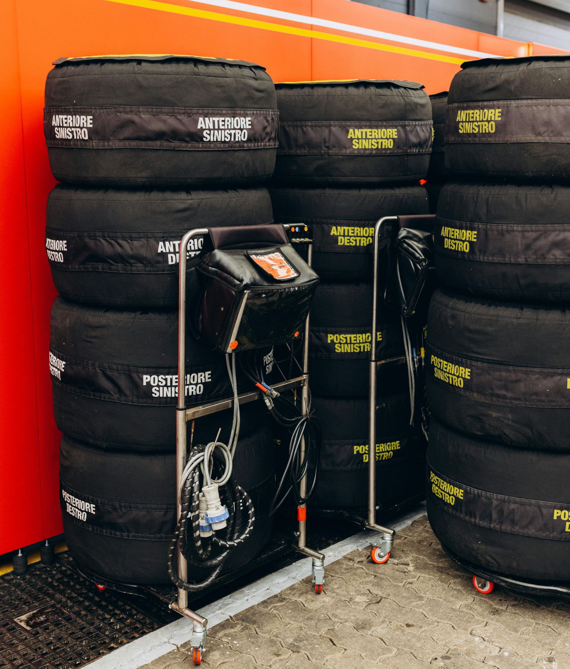 Tires with covers stacked near a cart with monitoring equipment inside a garage, possibly a race setting.