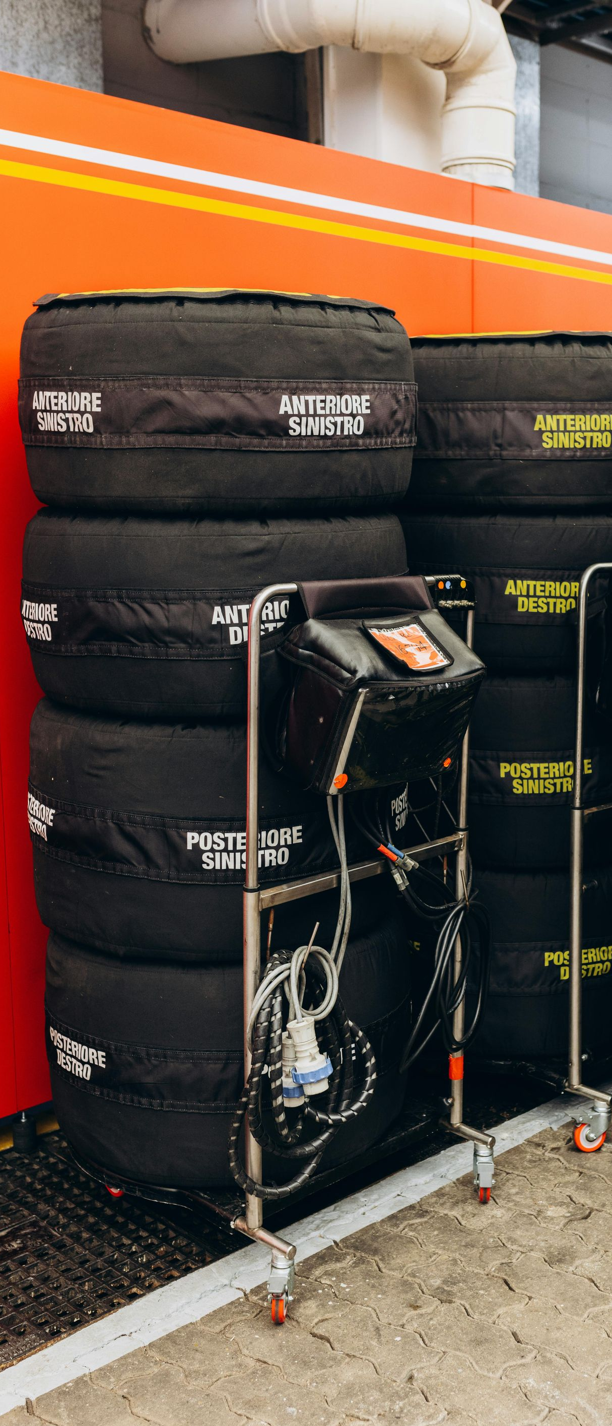 Stacks of black racing tires on metal carts inside a garage.