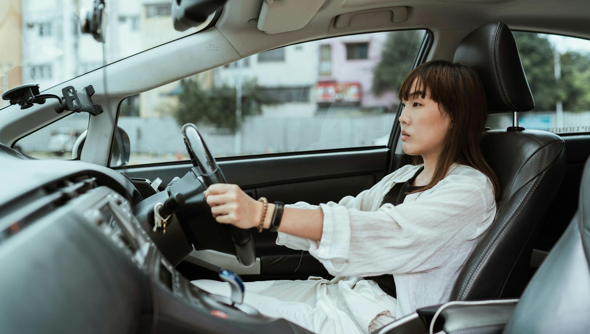 Woman driving a car, hands on the steering wheel, looking forward. Interior shot with sunlight.