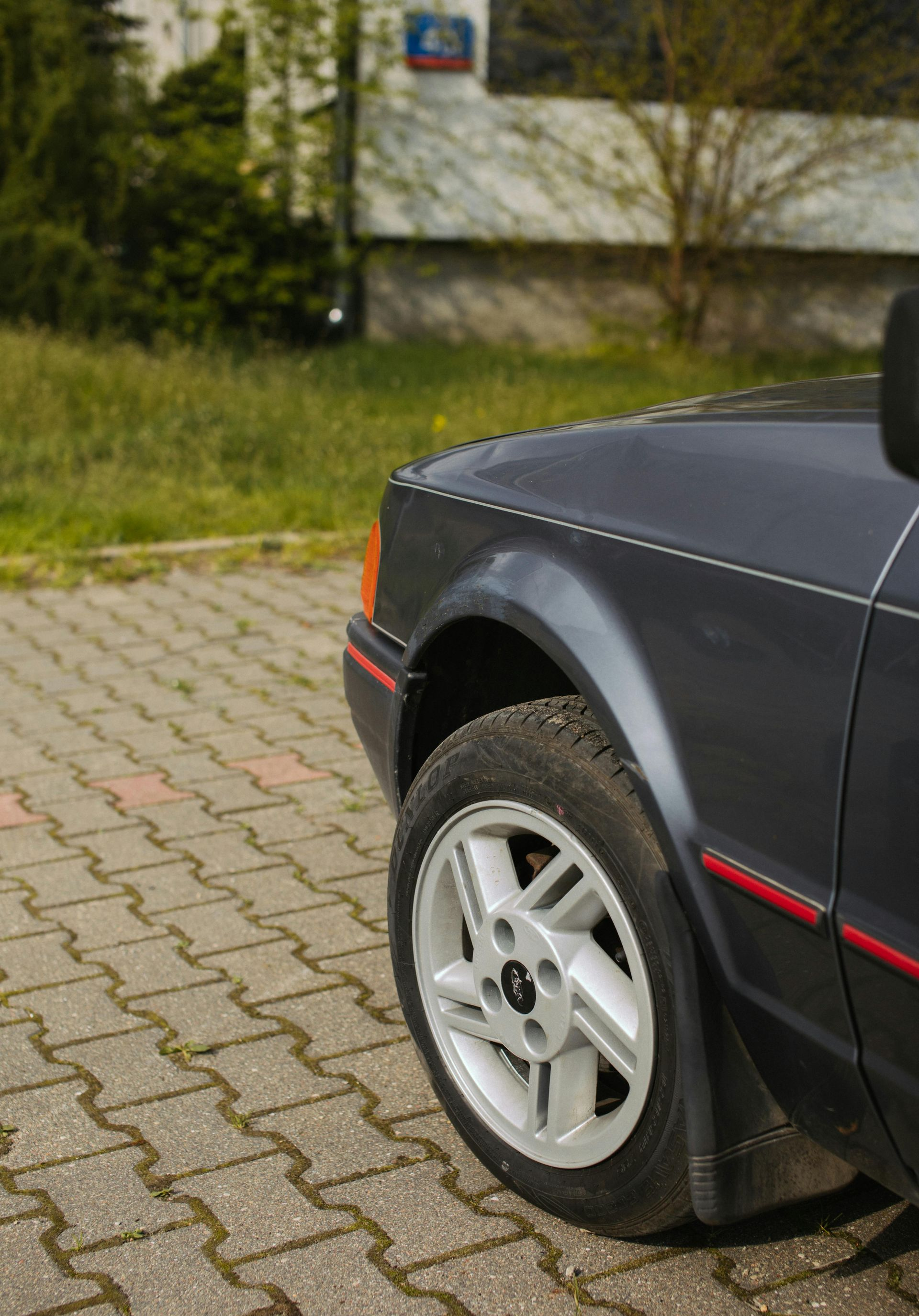 Dark gray Ford car's front quarter panel and wheel. Gray wheels, red trim, on a paved surface.
