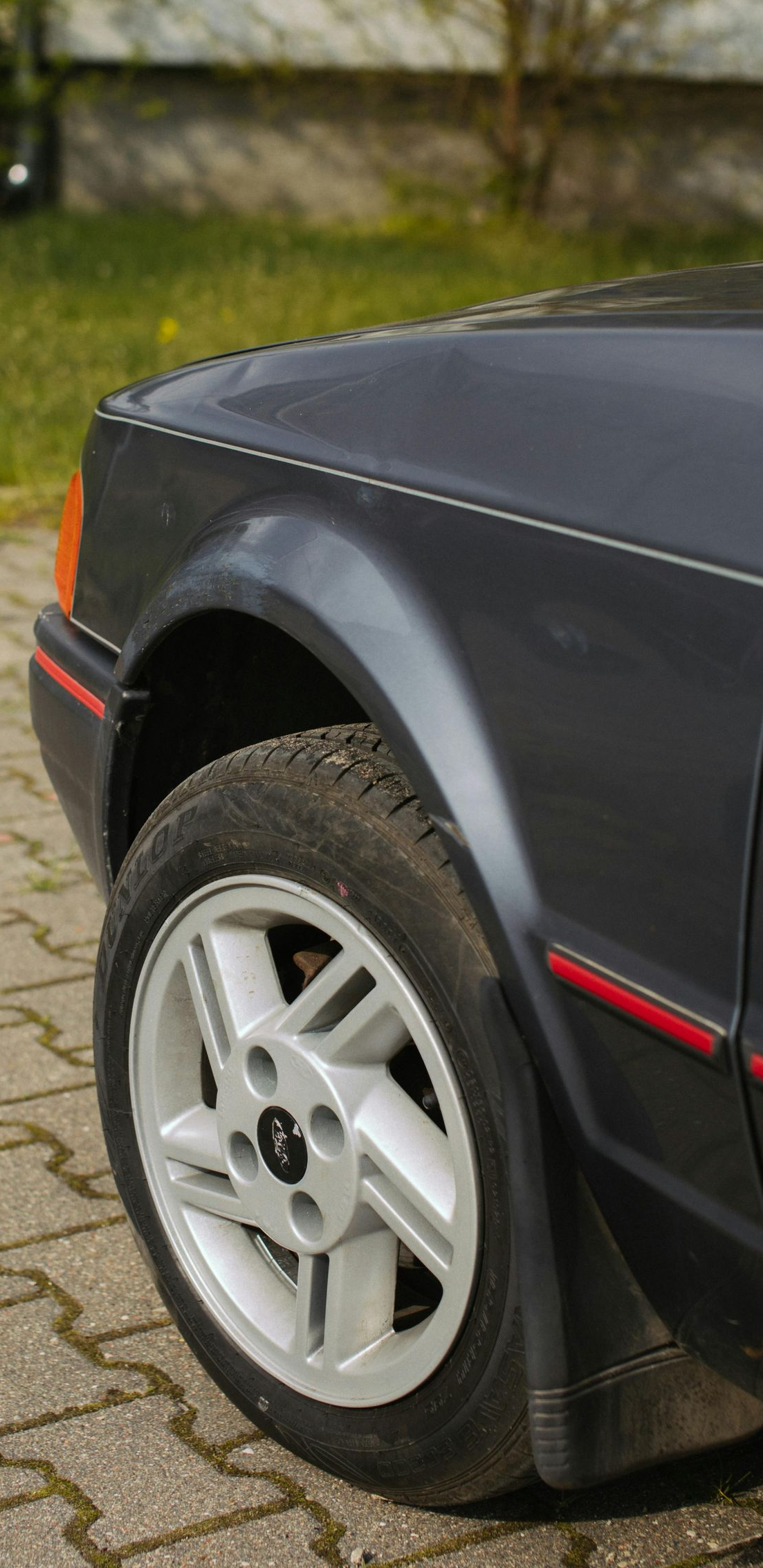Front quarter view of a dark gray car with a silver rim. Red detail along the car's body.