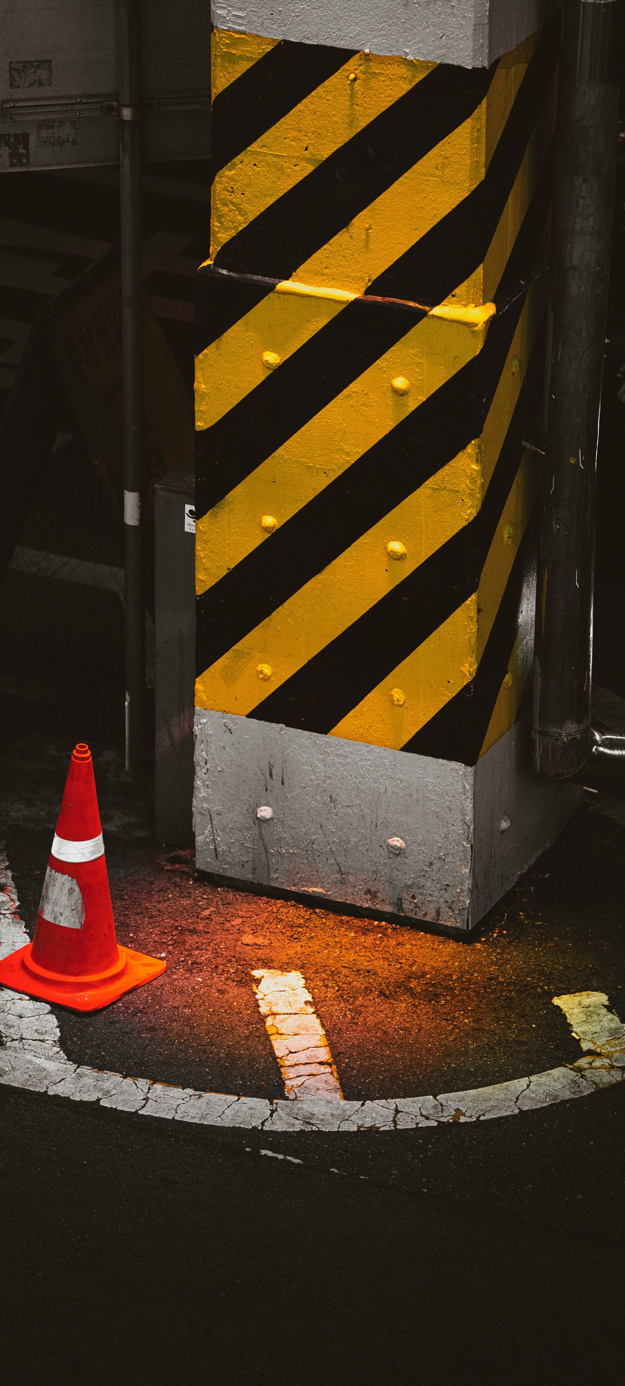 Black-and-yellow striped pillar with orange traffic cone at its base in a dim parking area