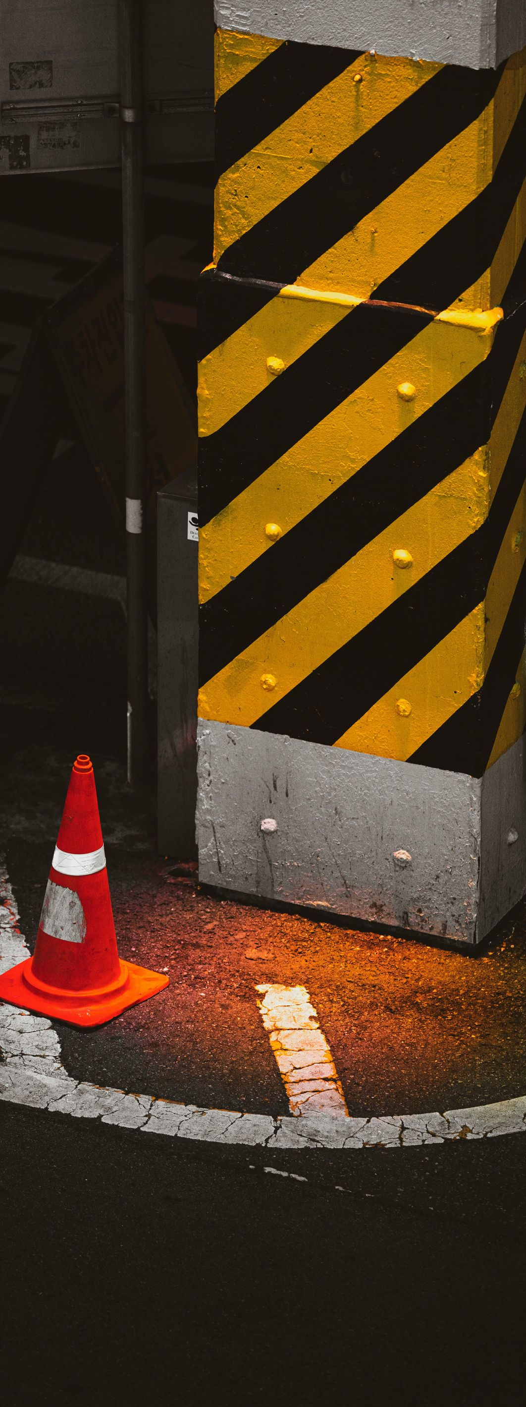 Black-and-yellow striped pillar with orange traffic cone at its base in a dim parking area